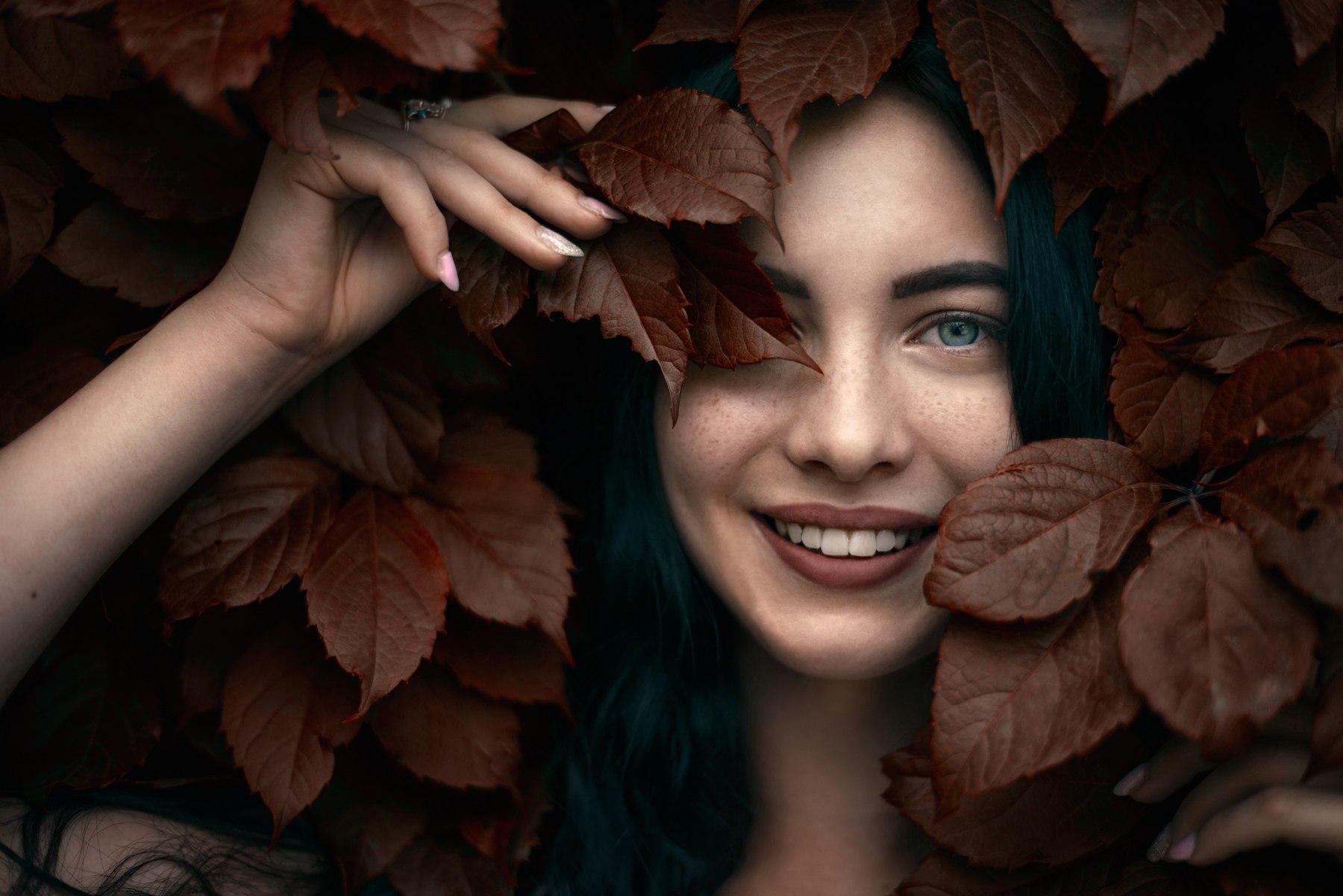 Woman with blue eyes smiling behind autumn leaves HD Wallpaper