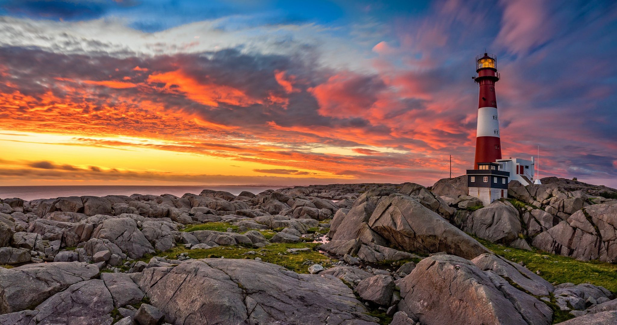 Lighthouse on rocky shore at sunset HD Wallpaper