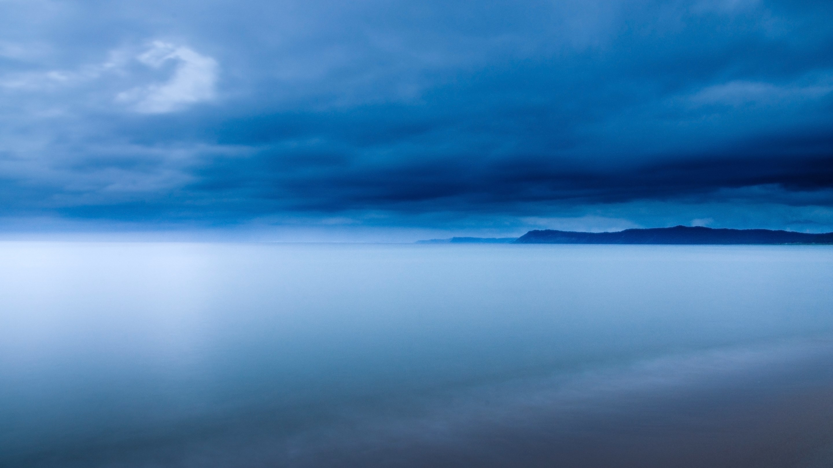 Dark clouds over a misty ocean and distant land HD Wallpaper