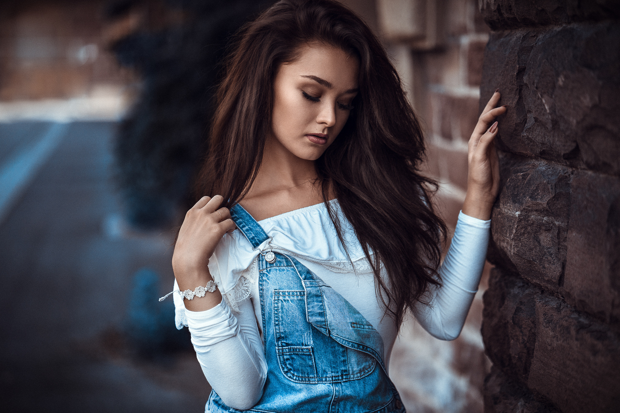 Woman in denim overalls leaning against a stone wall HD Wallpaper