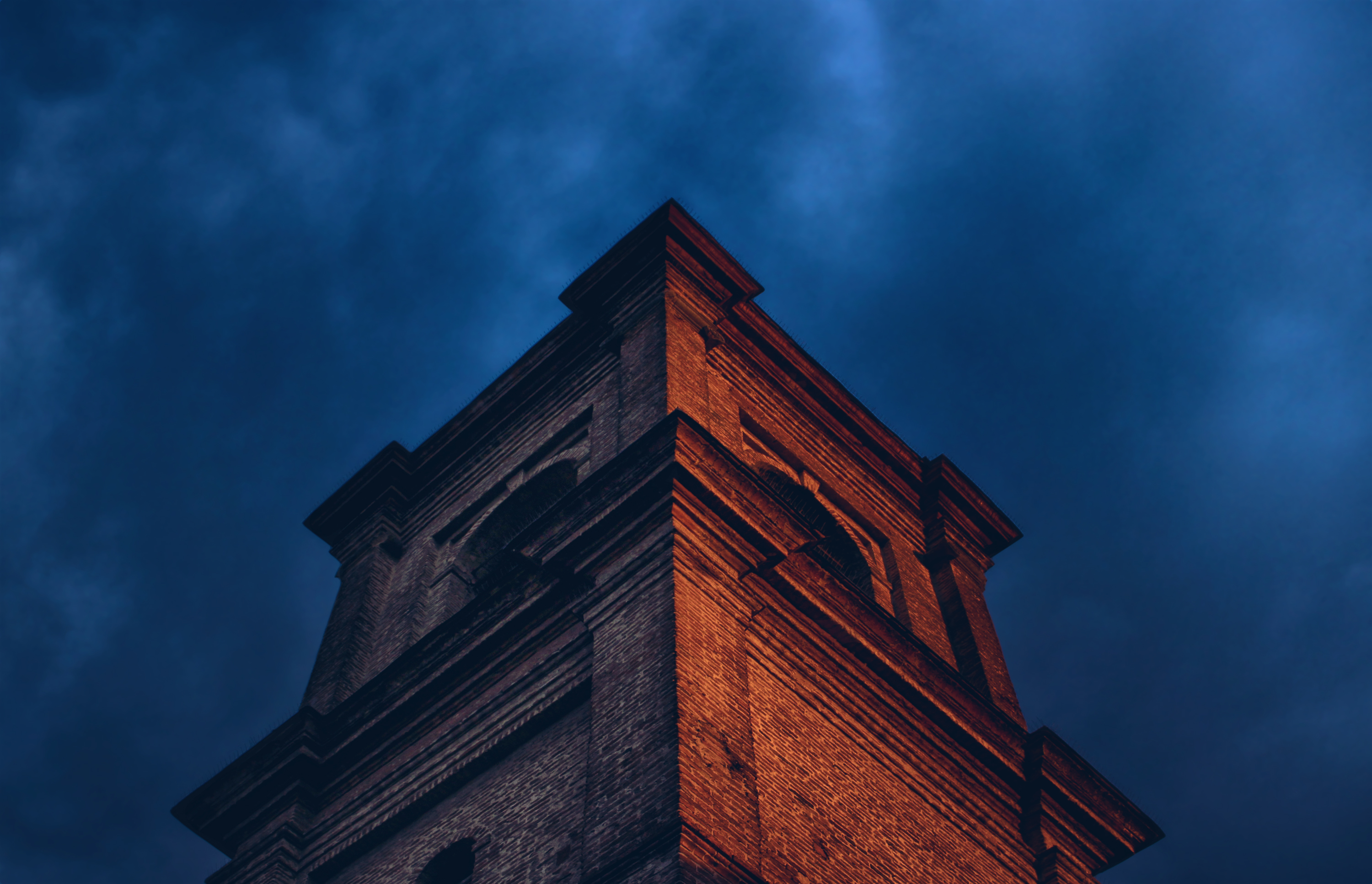 Brick tower against a dark blue cloudy sky HD Wallpaper