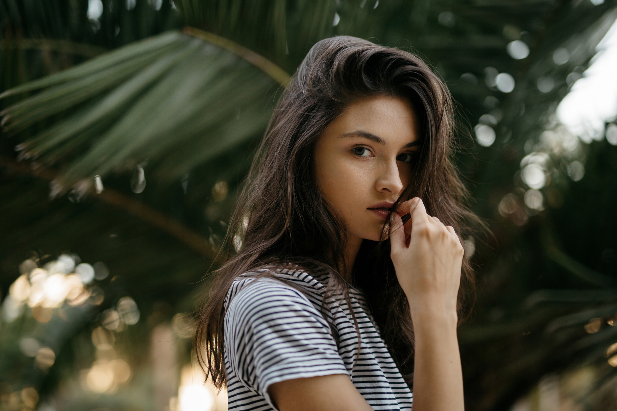 Woman with finger on lips in front of palm leaves HD Wallpaper