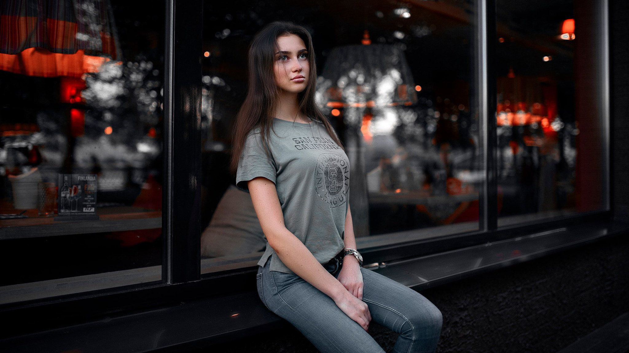 Woman in T-shirt and jeans sitting by a window HD Wallpaper