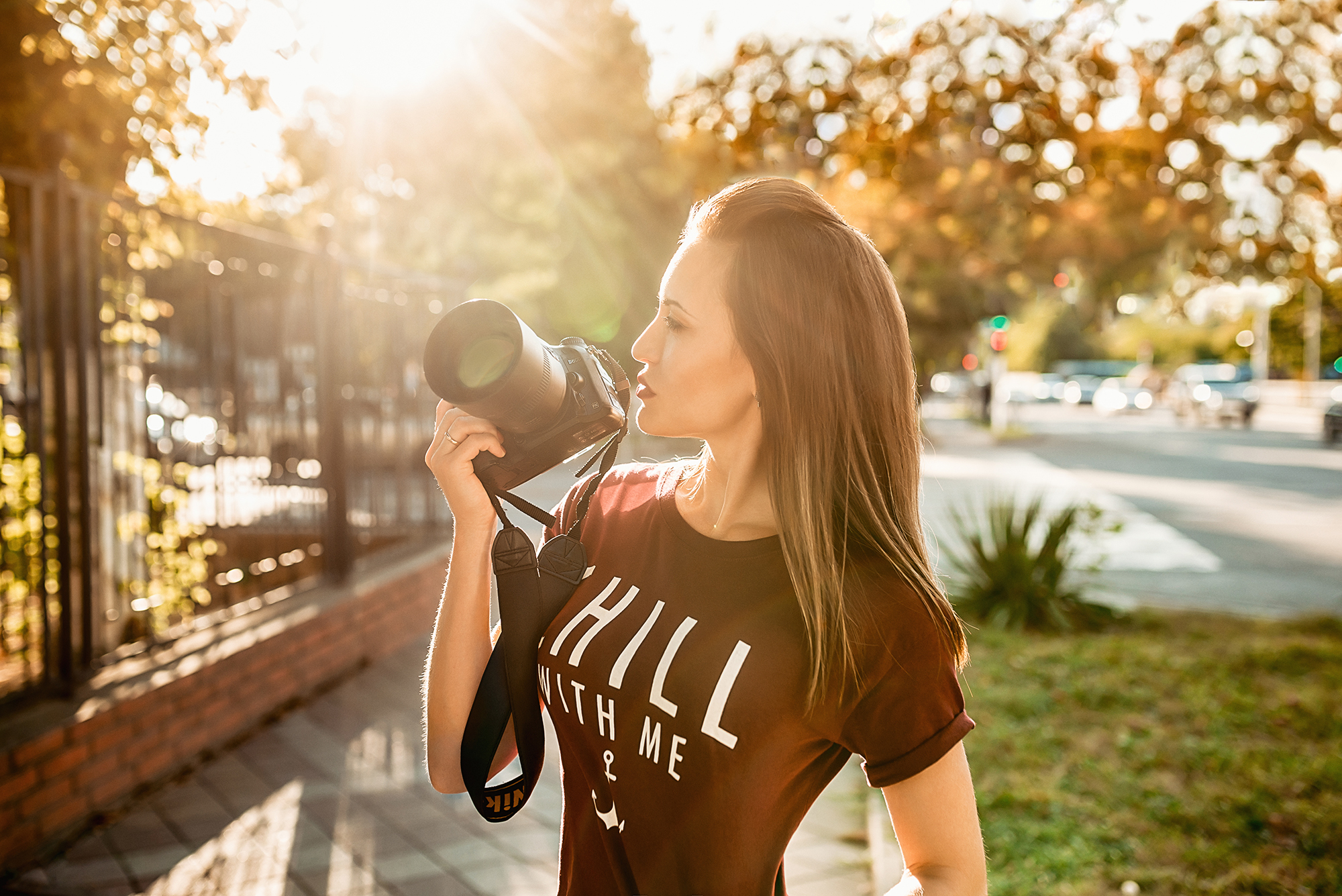 Woman holding a Nikon camera outdoors at sunset HD Wallpaper