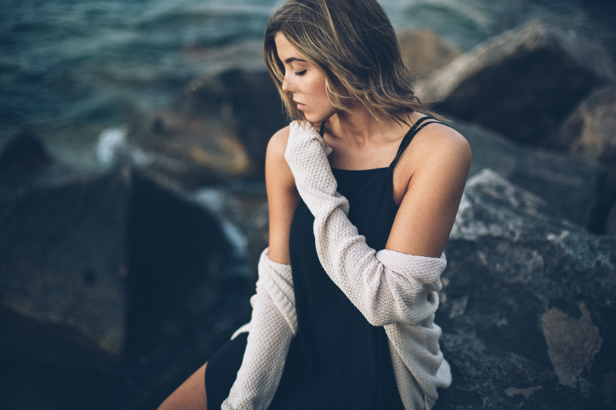 Woman in black dress and cardigan sitting on rocks HD Wallpaper