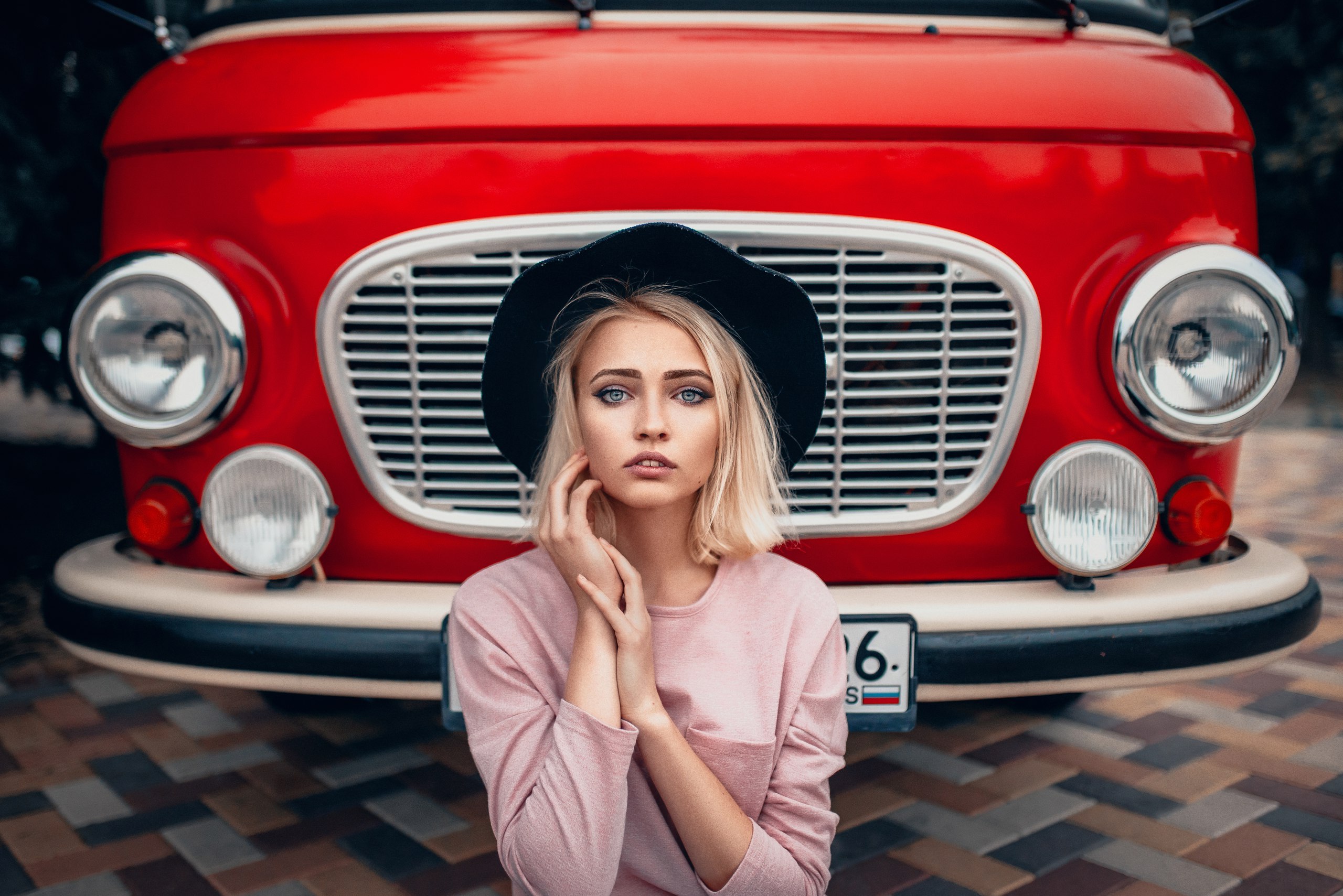 Woman with blonde hair and blue eyes wearing a hat in front of a red Barkas HD Wallpaper