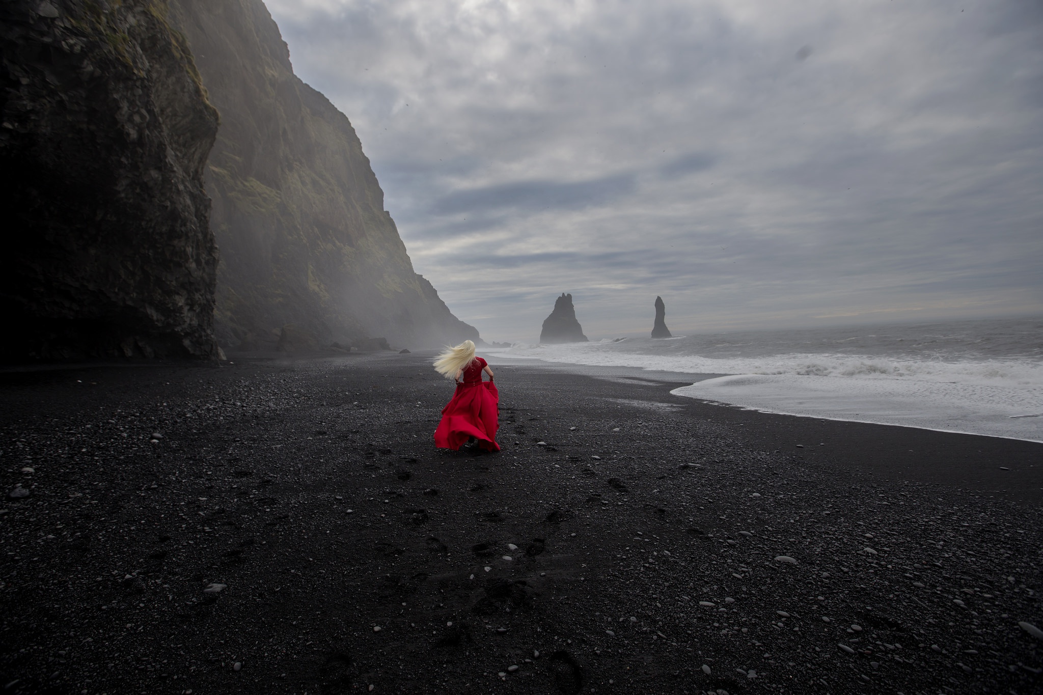 Woman in red dress on black sand beach with sea stacks HD Wallpaper