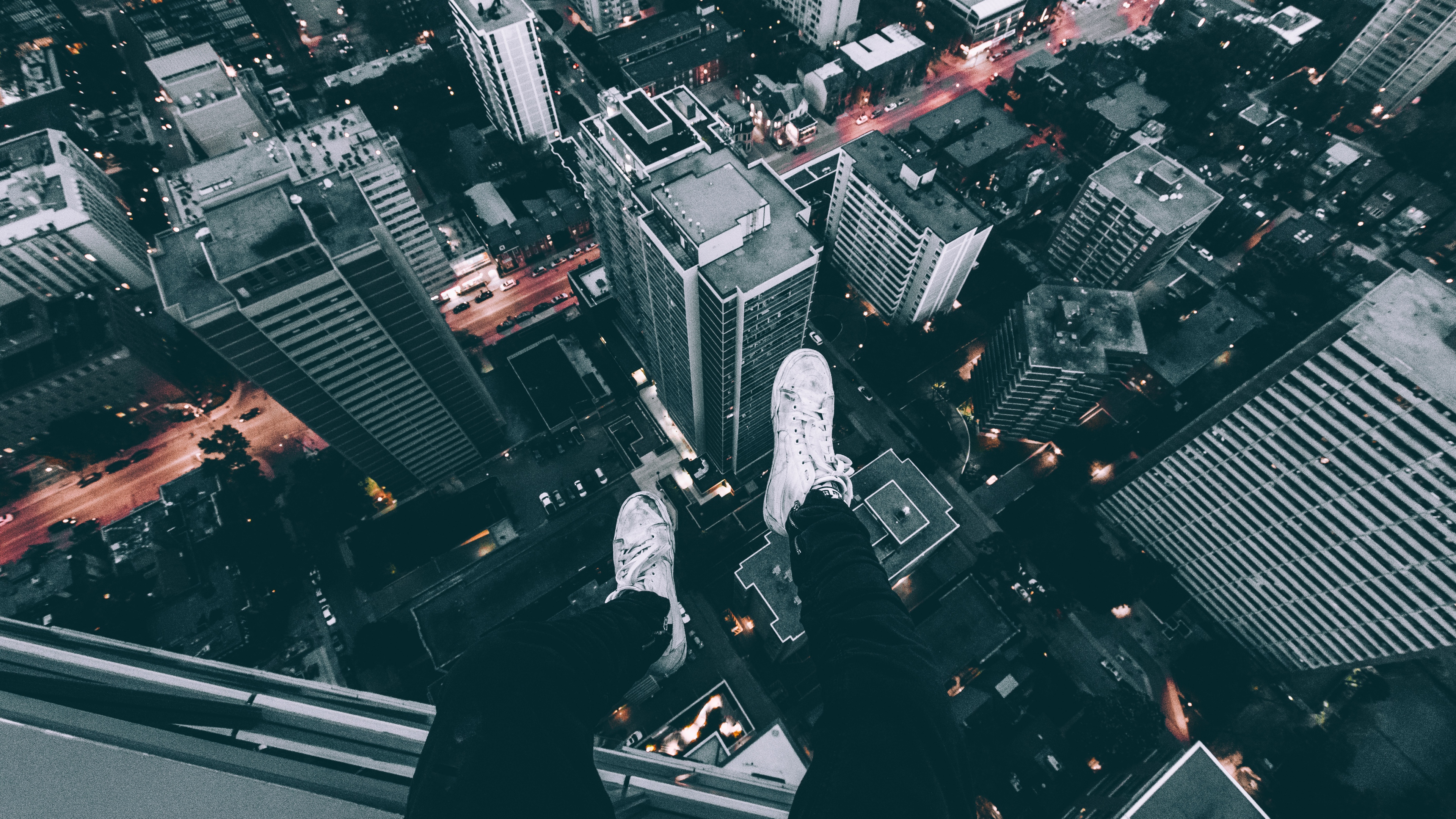Person's legs hanging over a cityscape at night HD Wallpaper