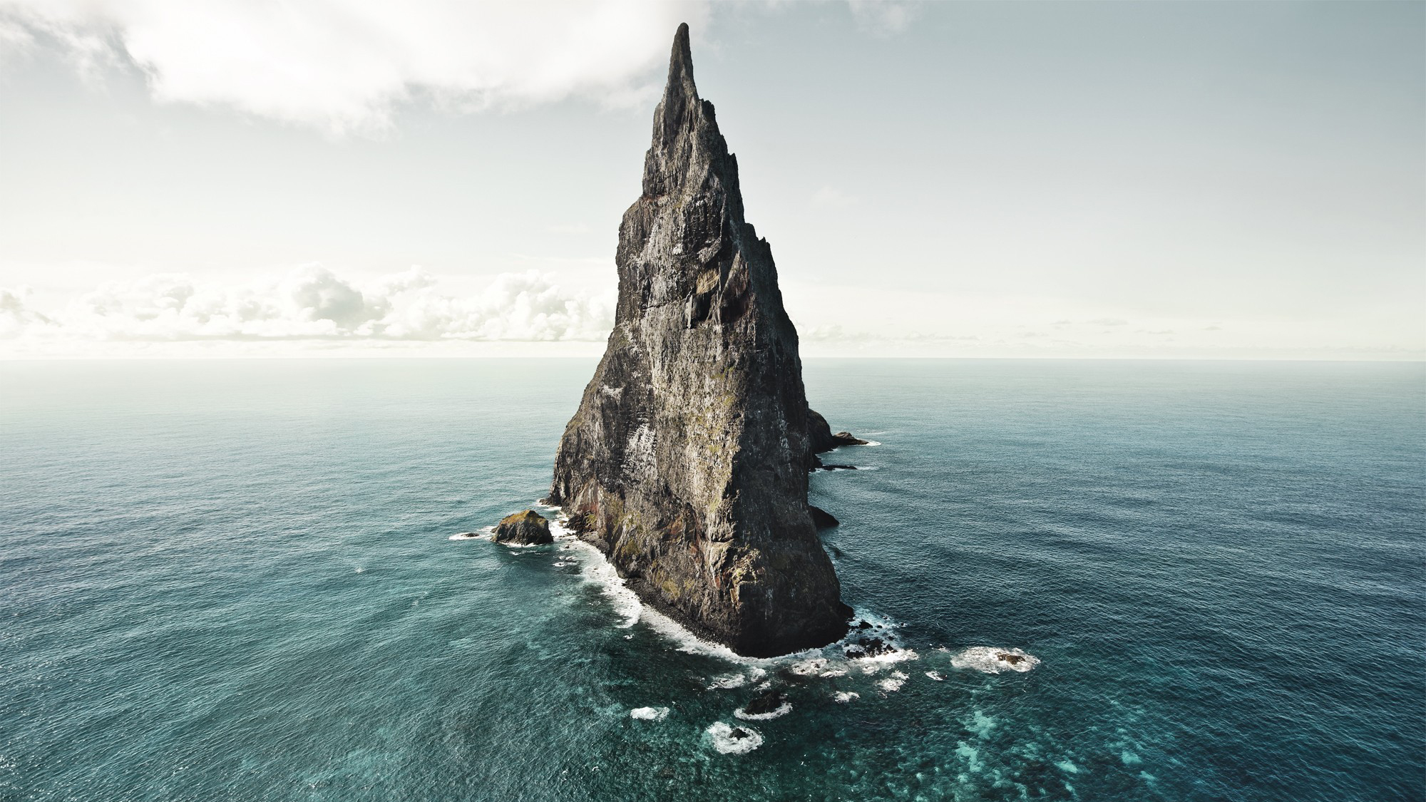 Jagged rock formation in the sea under a cloudy sky HD Wallpaper