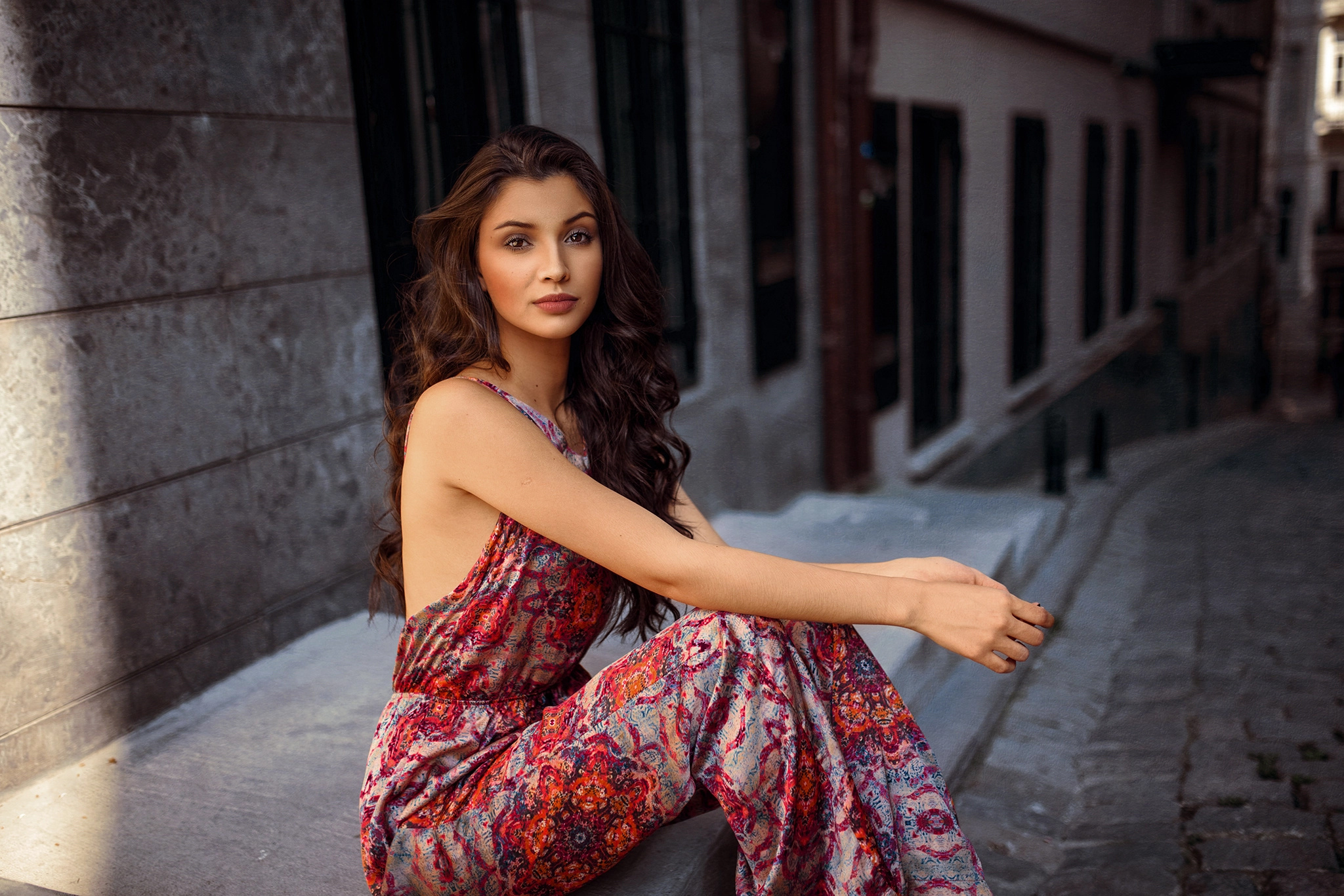 Woman in patterned jumpsuit sitting on steps HD Wallpaper
