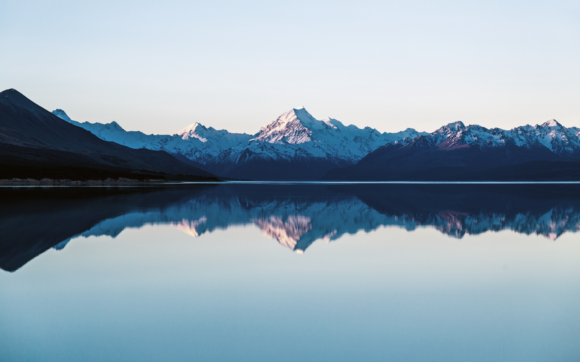Snow-capped mountains reflected in a calm lake at sunrise HD Wallpaper