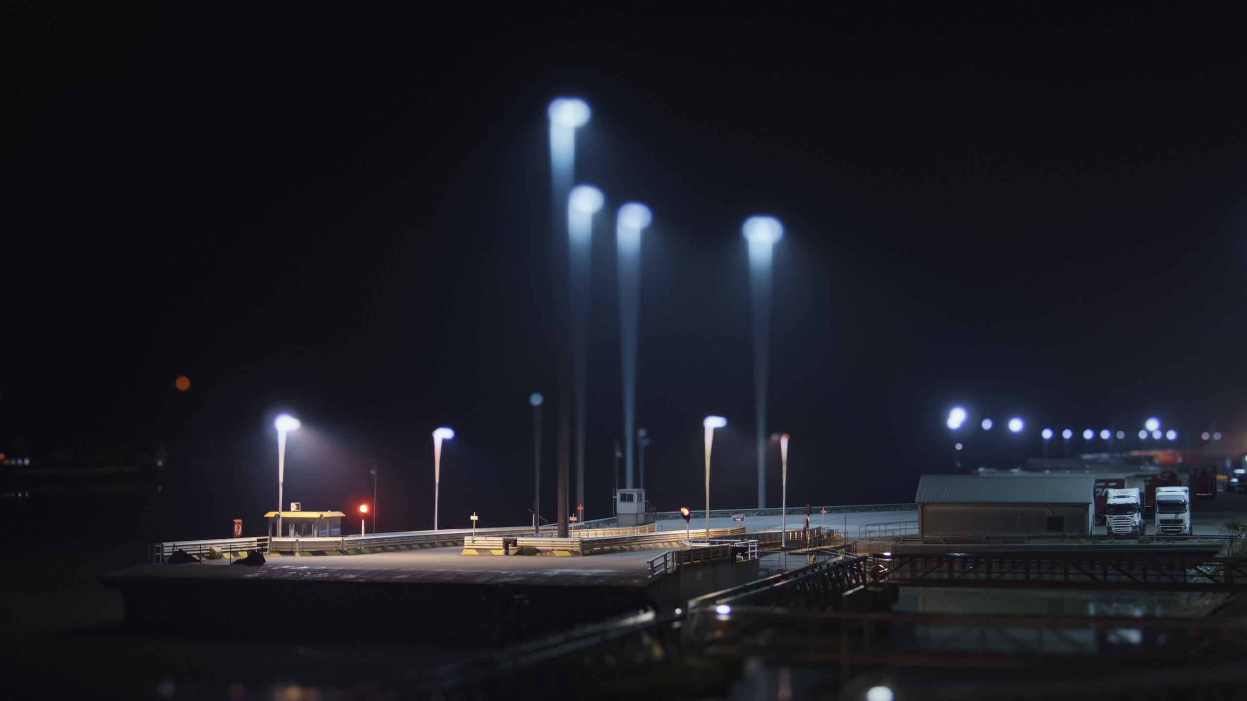 Nighttime industrial dock with bright lights and trucks HD Wallpaper