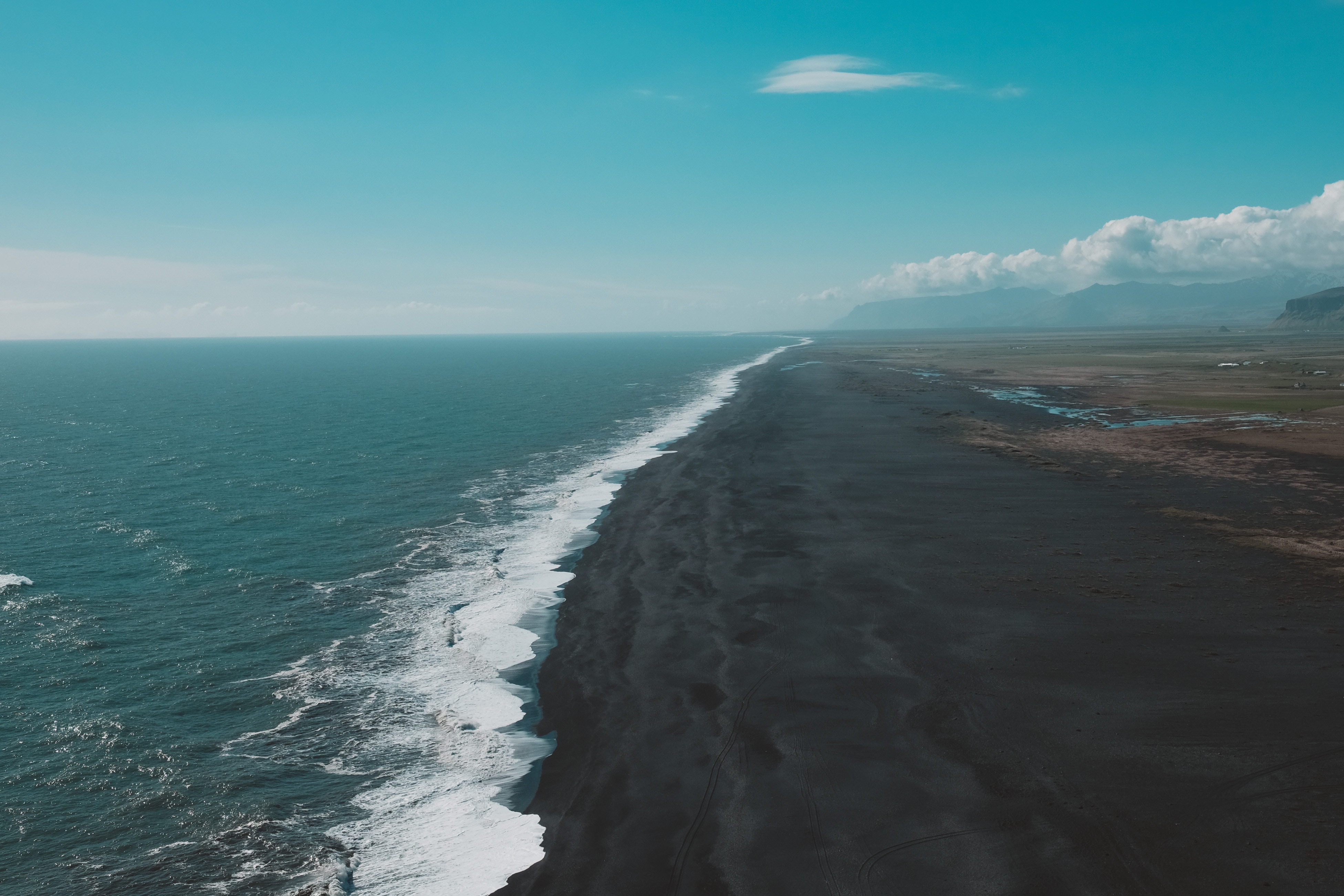 Black sand beach with ocean waves and distant mountains HD Wallpaper