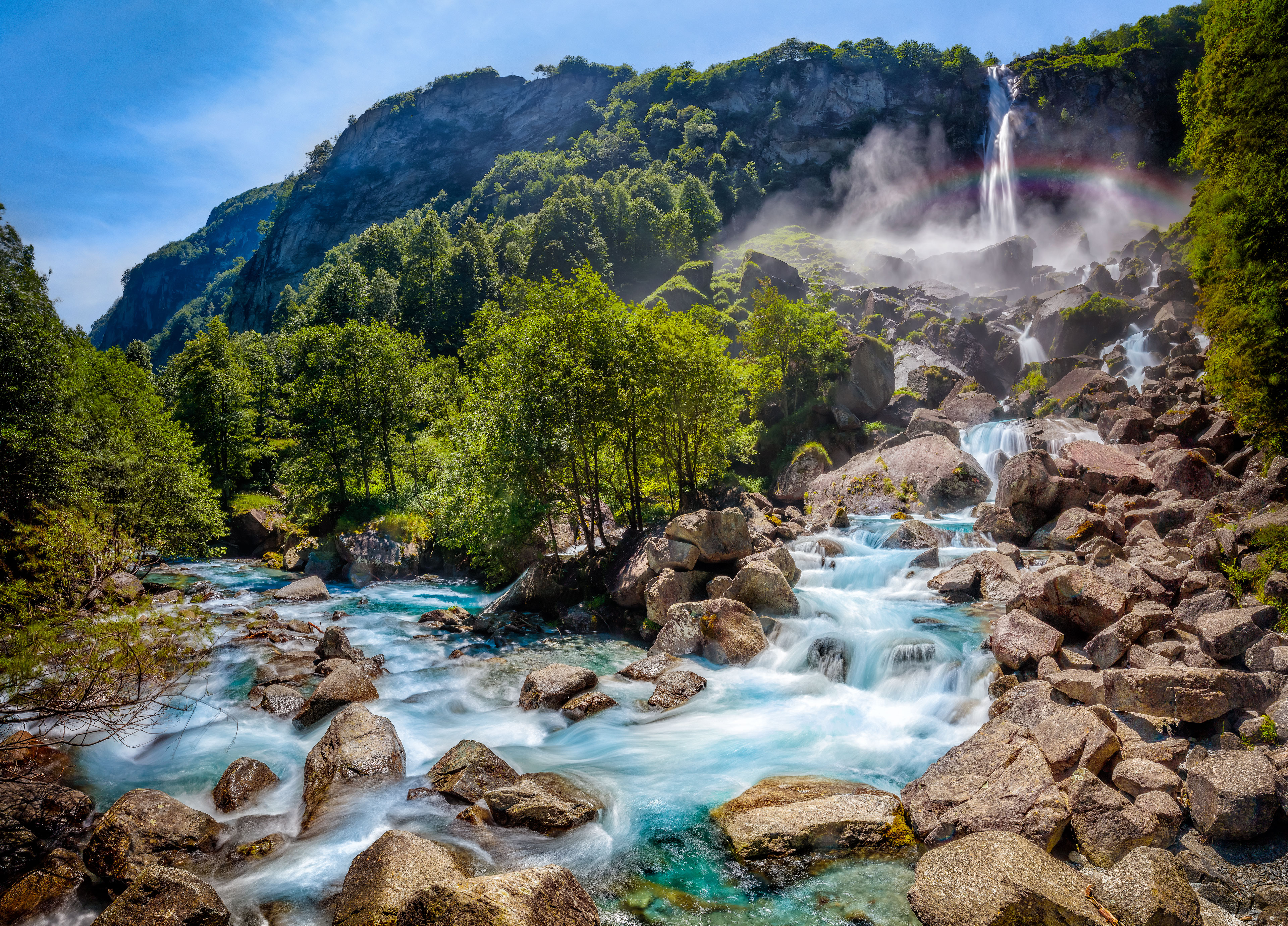 Waterfall cascading over rocks in a lush green mountain landscape HD Wallpaper