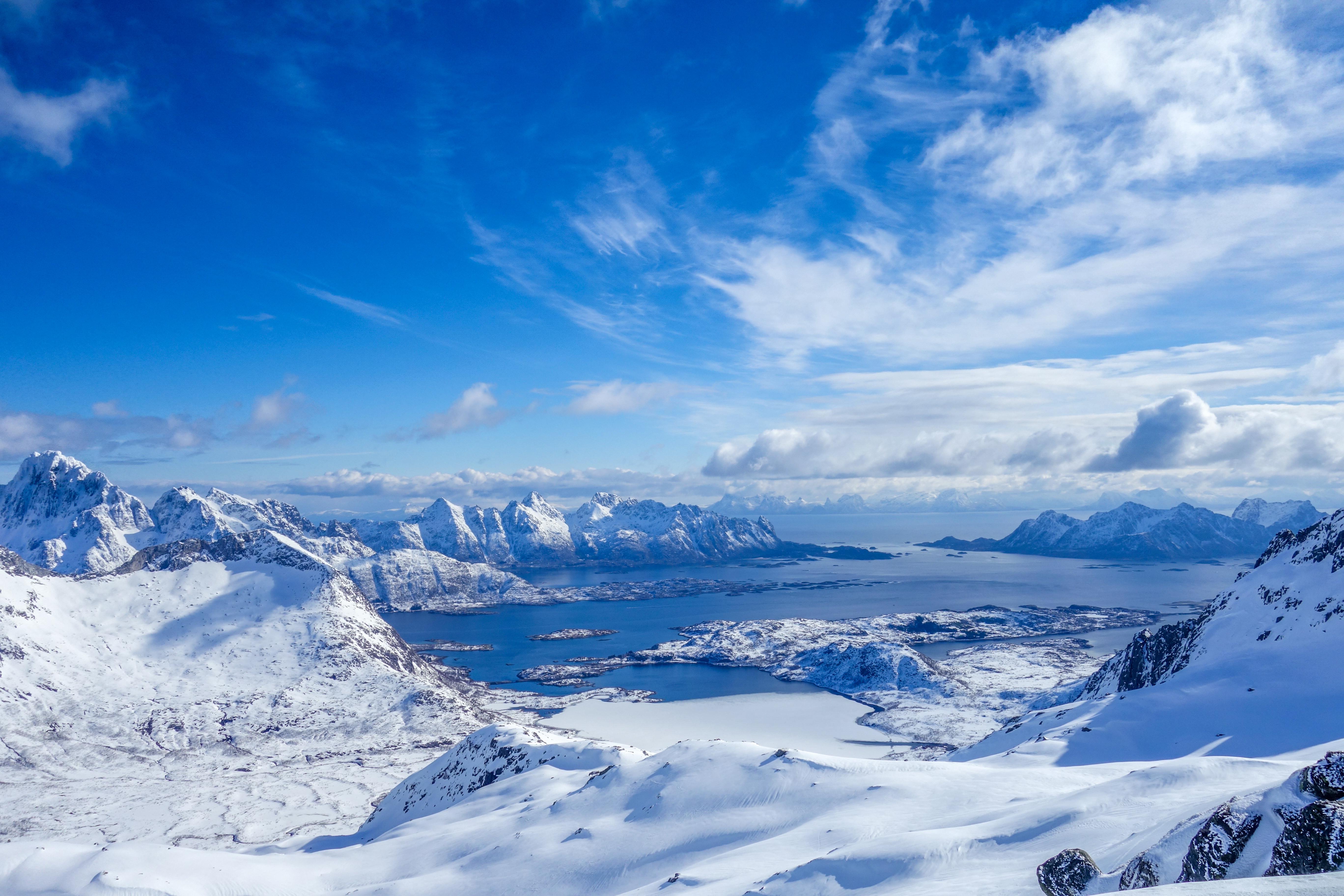 Snowy mountains and a blue bay under a cloudy sky HD Wallpaper