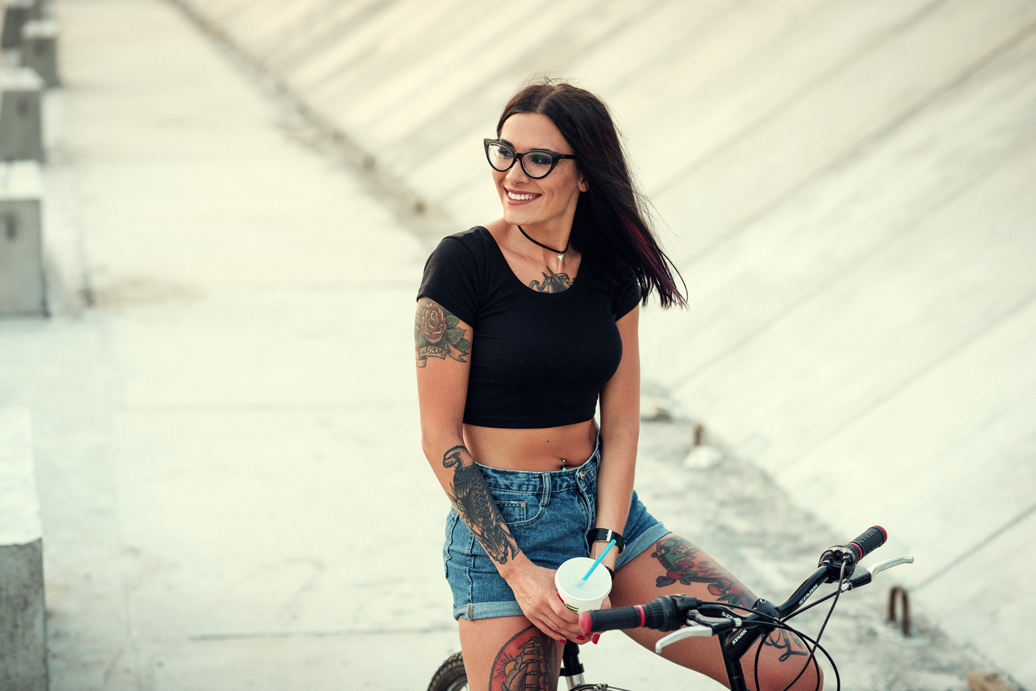 Woman with tattoos on a bicycle holding a drink HD Wallpaper