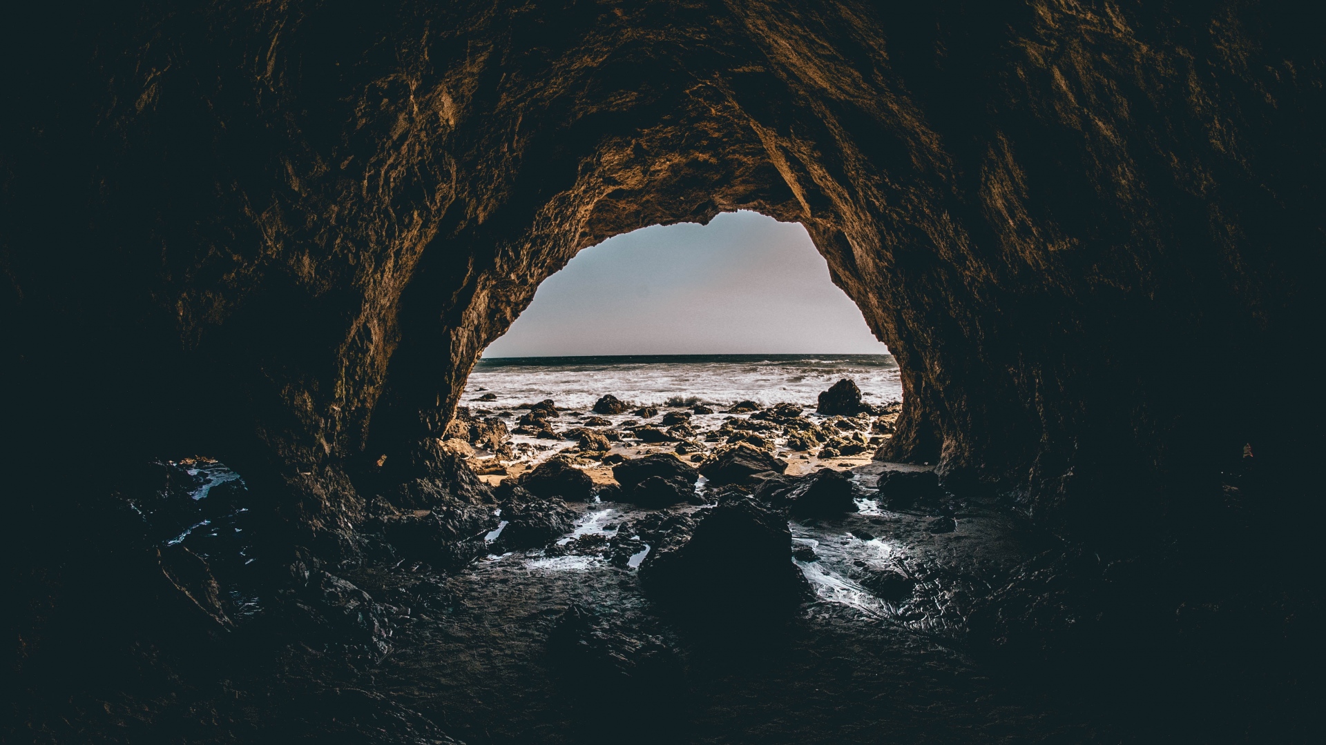 View of the ocean through a dark cave entrance HD Wallpaper