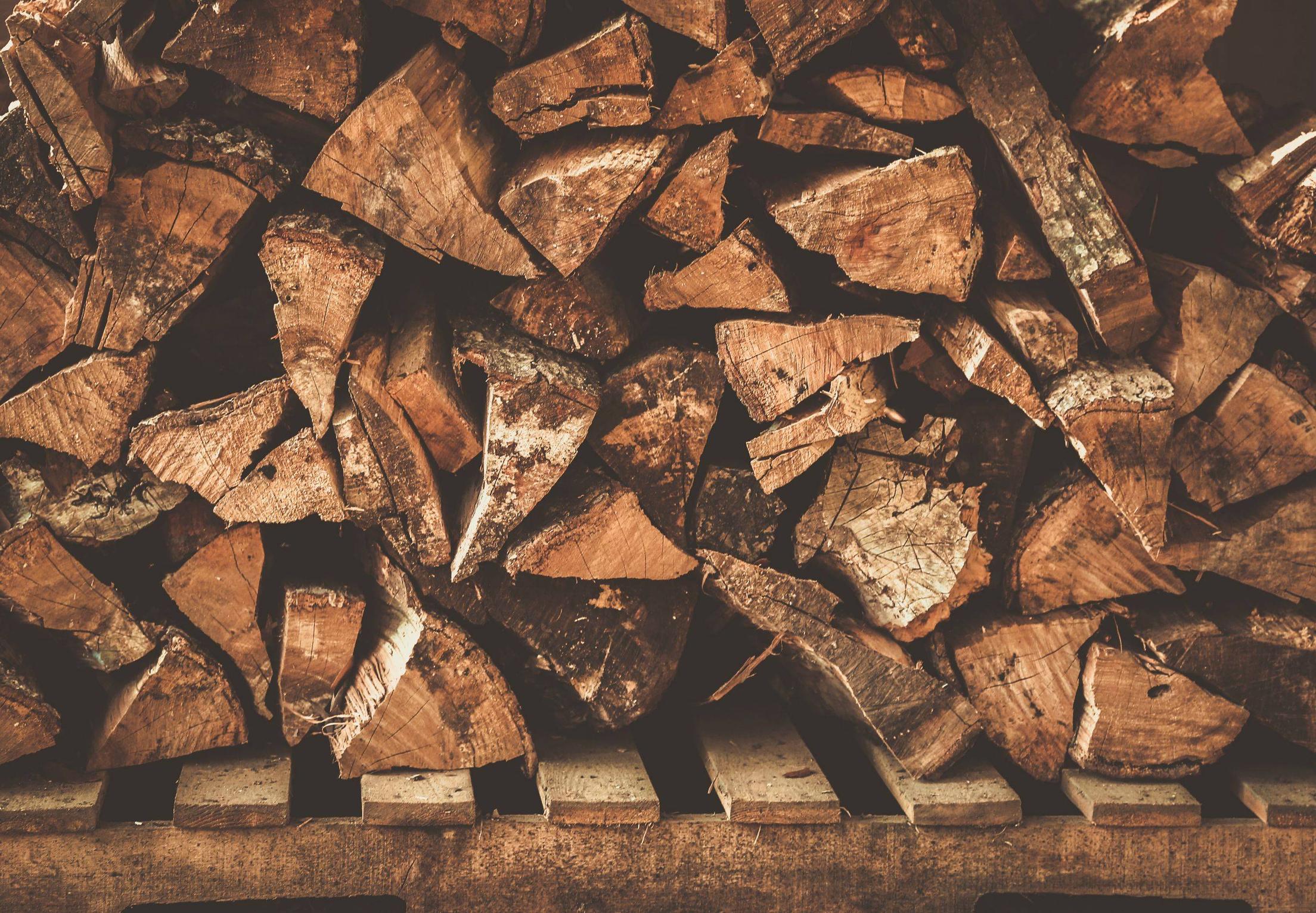 Pile of chopped firewood stacked on wooden planks HD Wallpaper