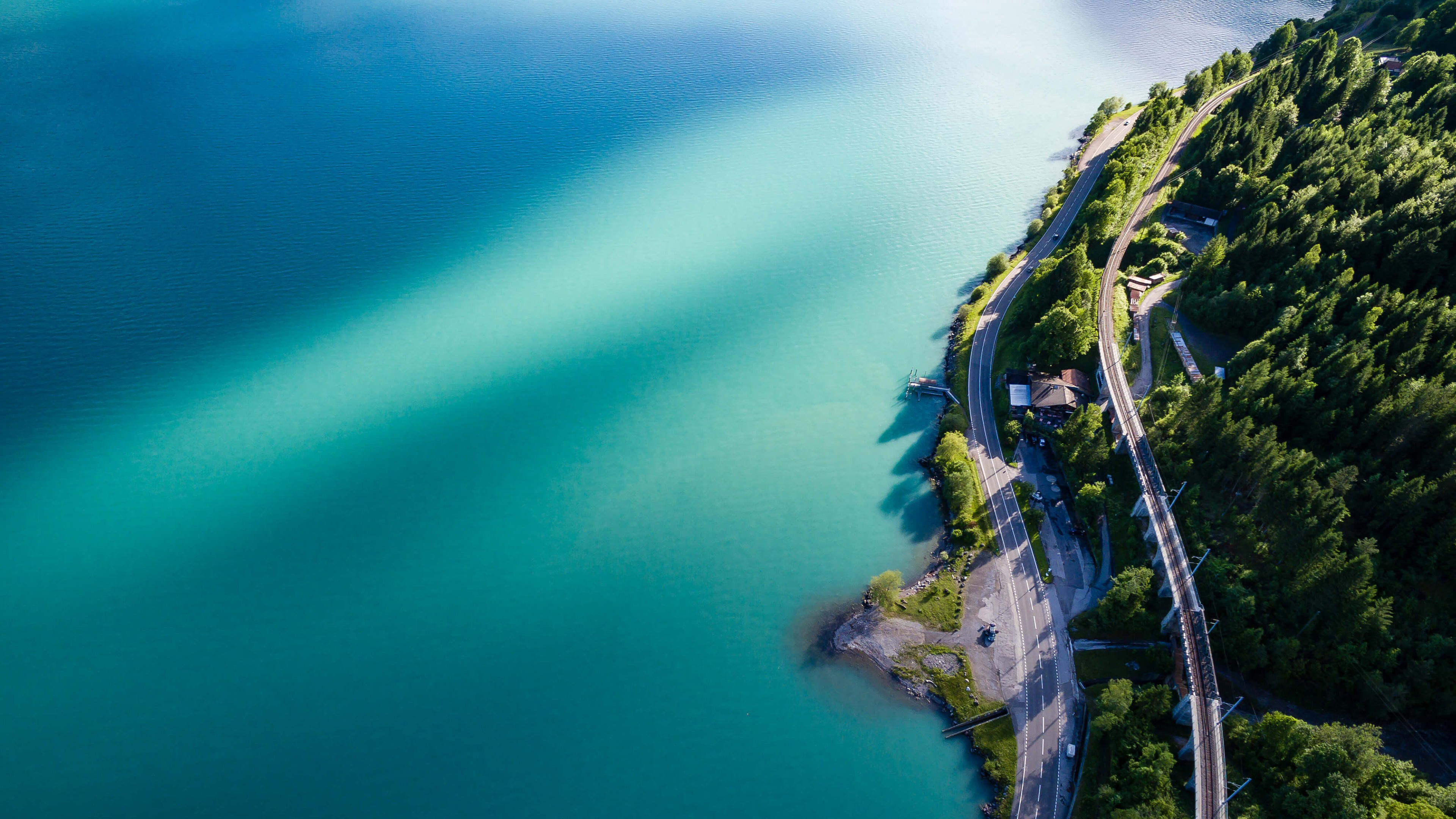 Aerial view of a turquoise lake with a road and railway HD Wallpaper