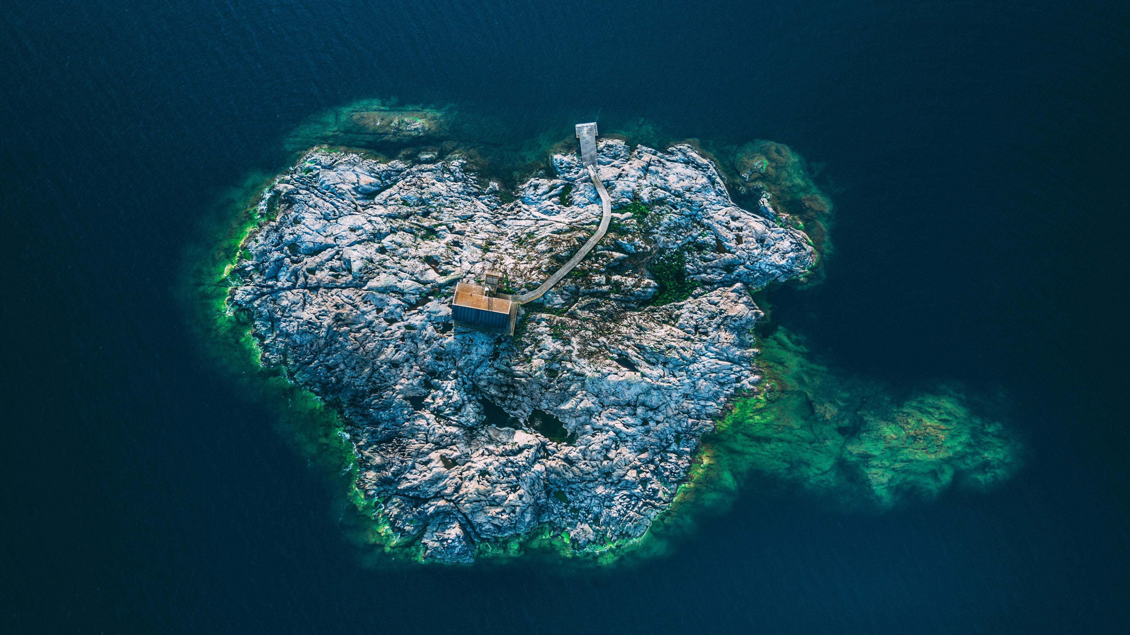 Aerial view of a rocky island with a small building and pier HD Wallpaper