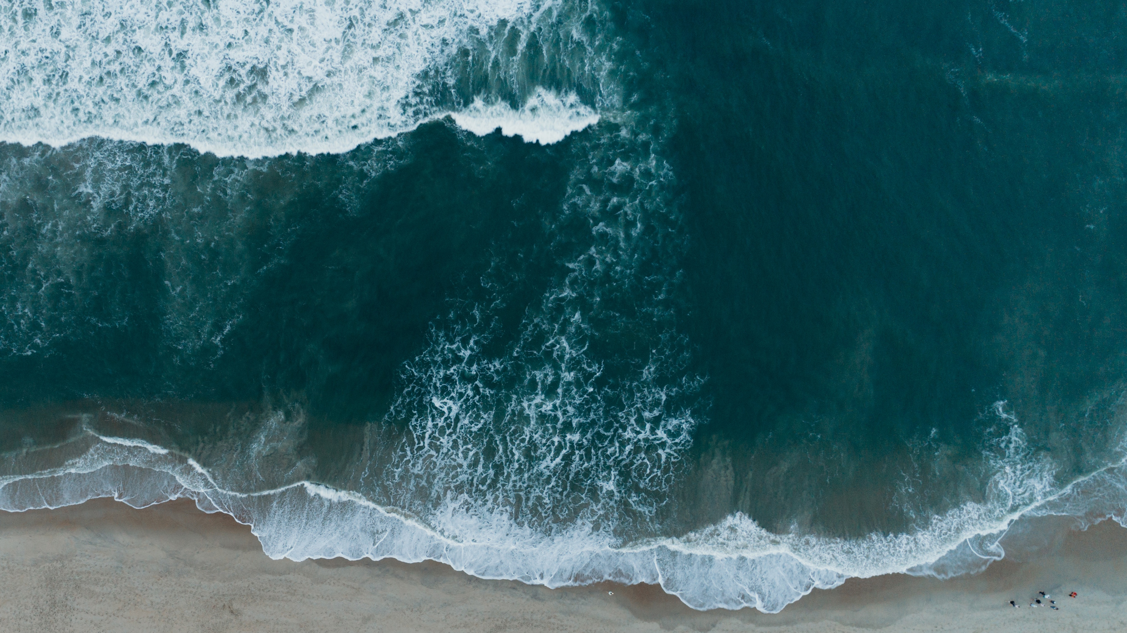 Aerial view of ocean waves crashing on a sandy beach HD Wallpaper
