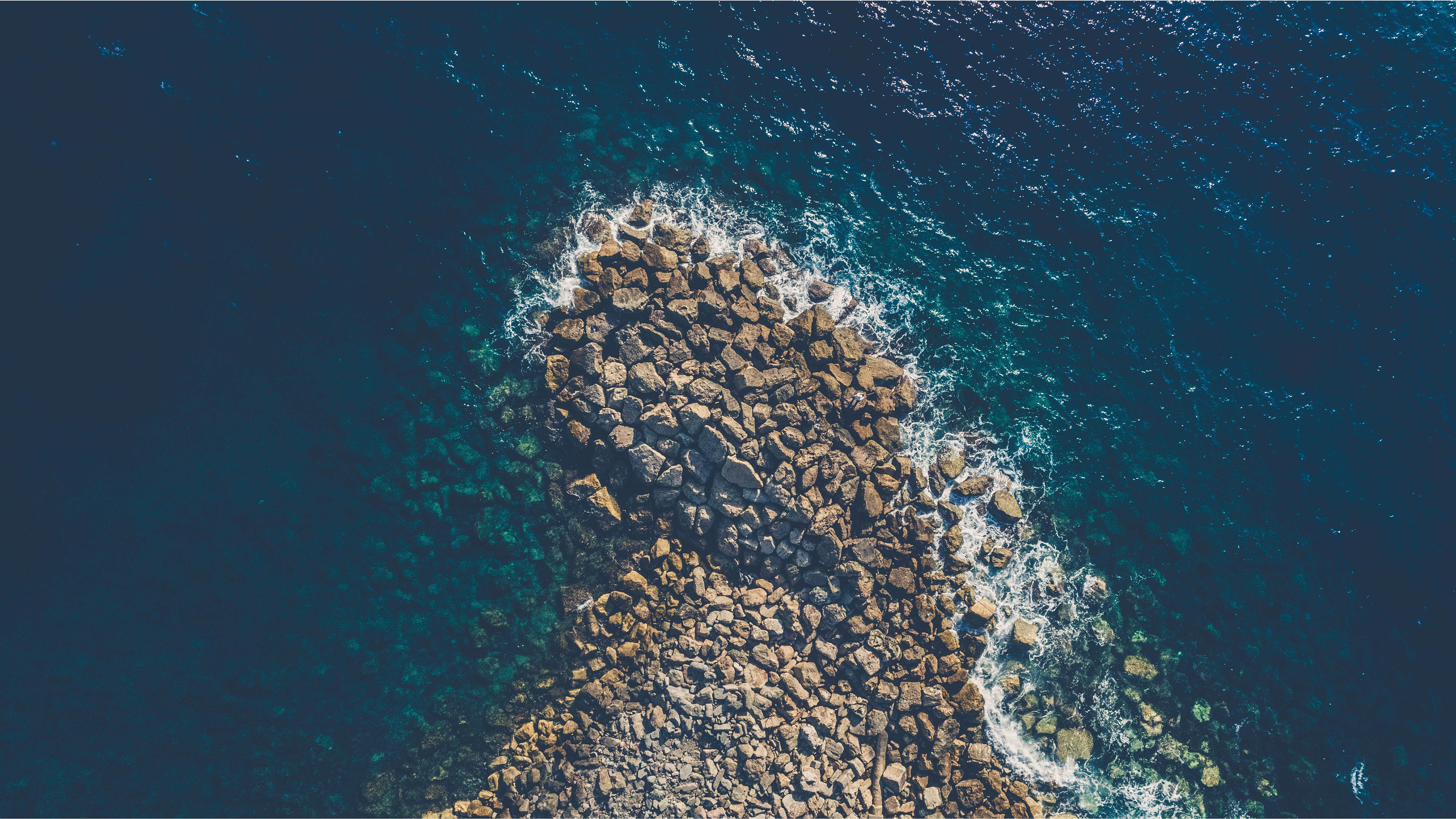 Aerial view of rocky coastline with dark blue sea HD Wallpaper