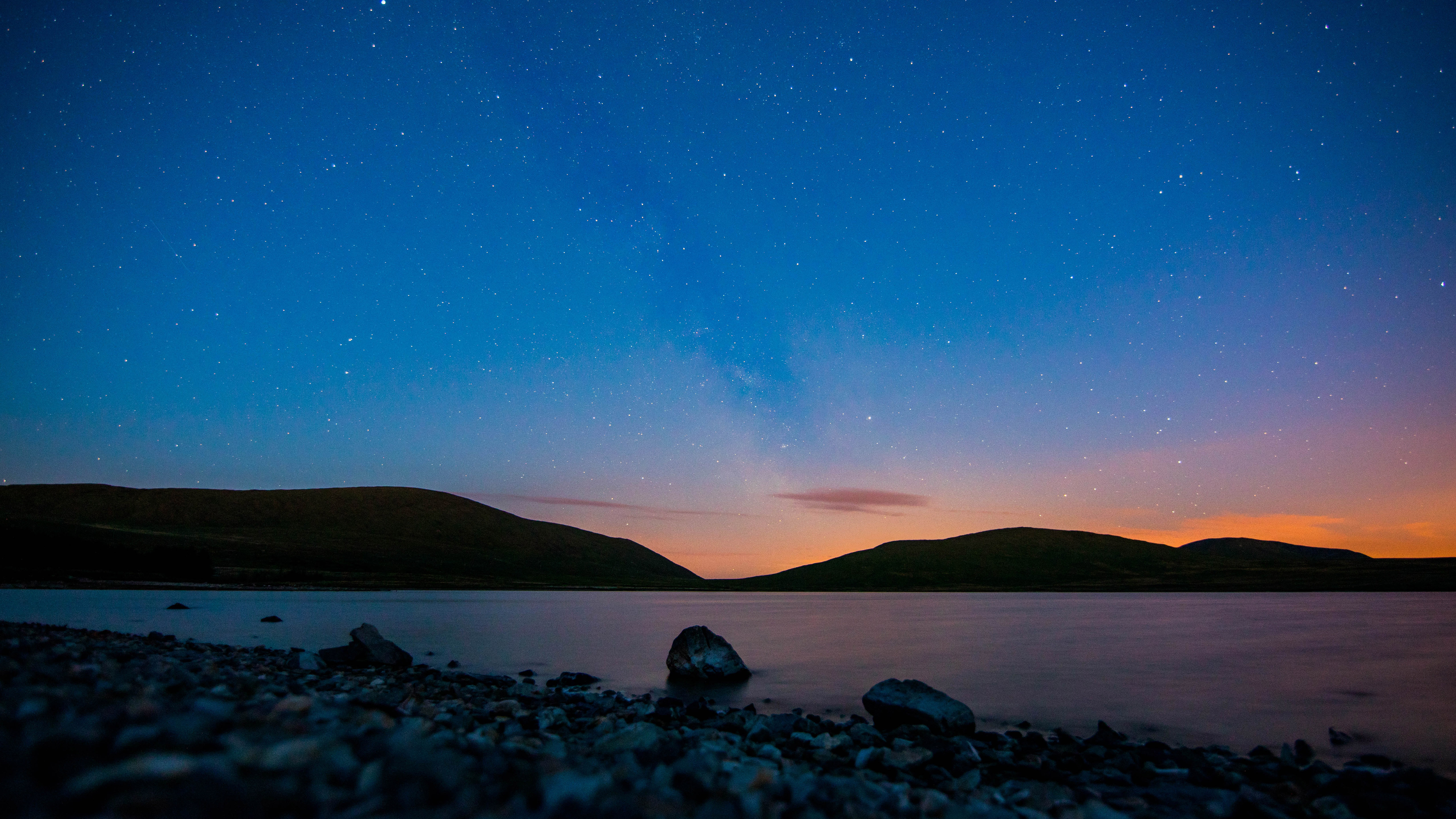 Night sky over a lake with hills and rocks HD Wallpaper