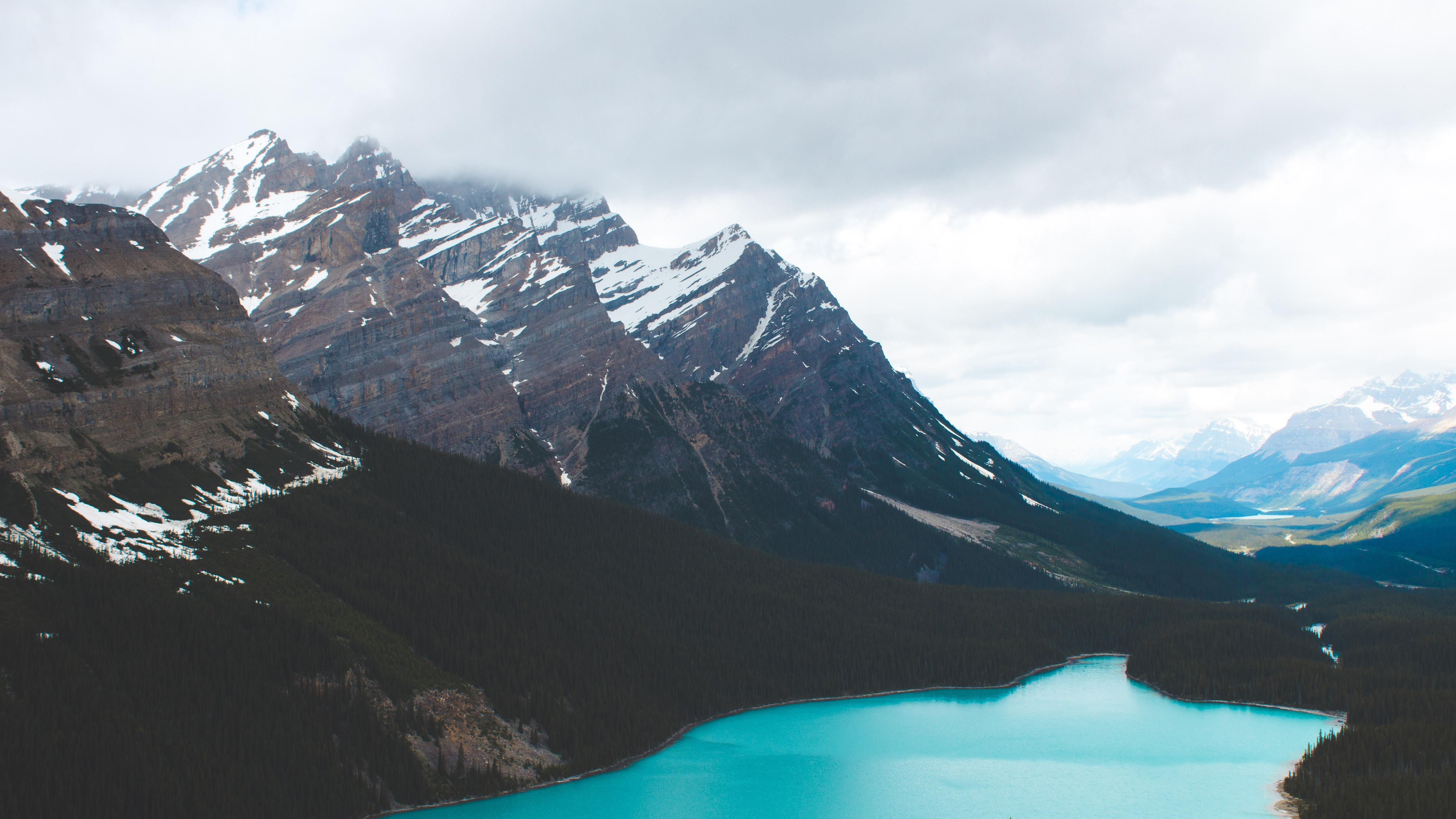 Snowy mountains overlooking a turquoise lake and forest HD Wallpaper