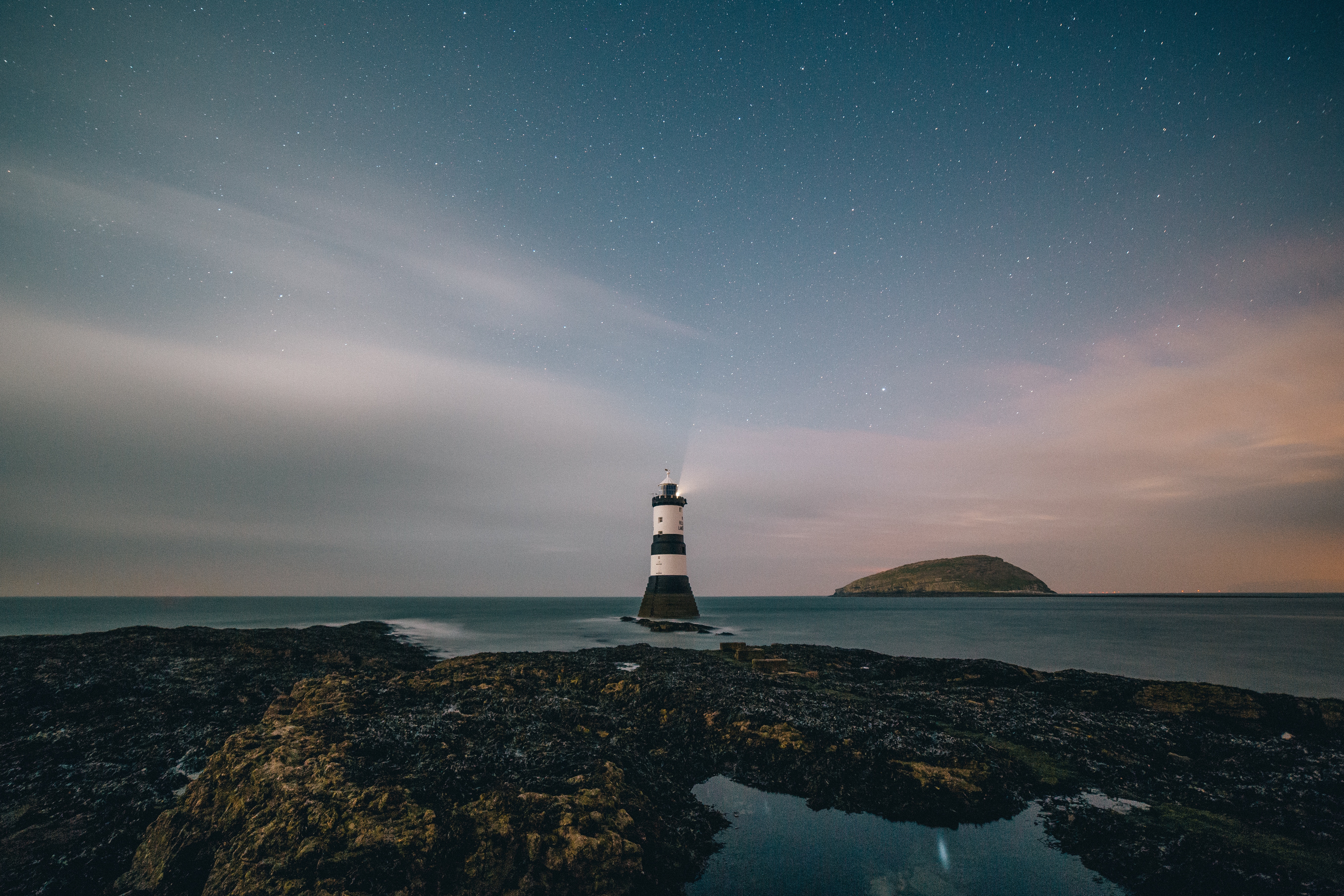 Lighthouse on rocky shore under starry sky HD Wallpaper