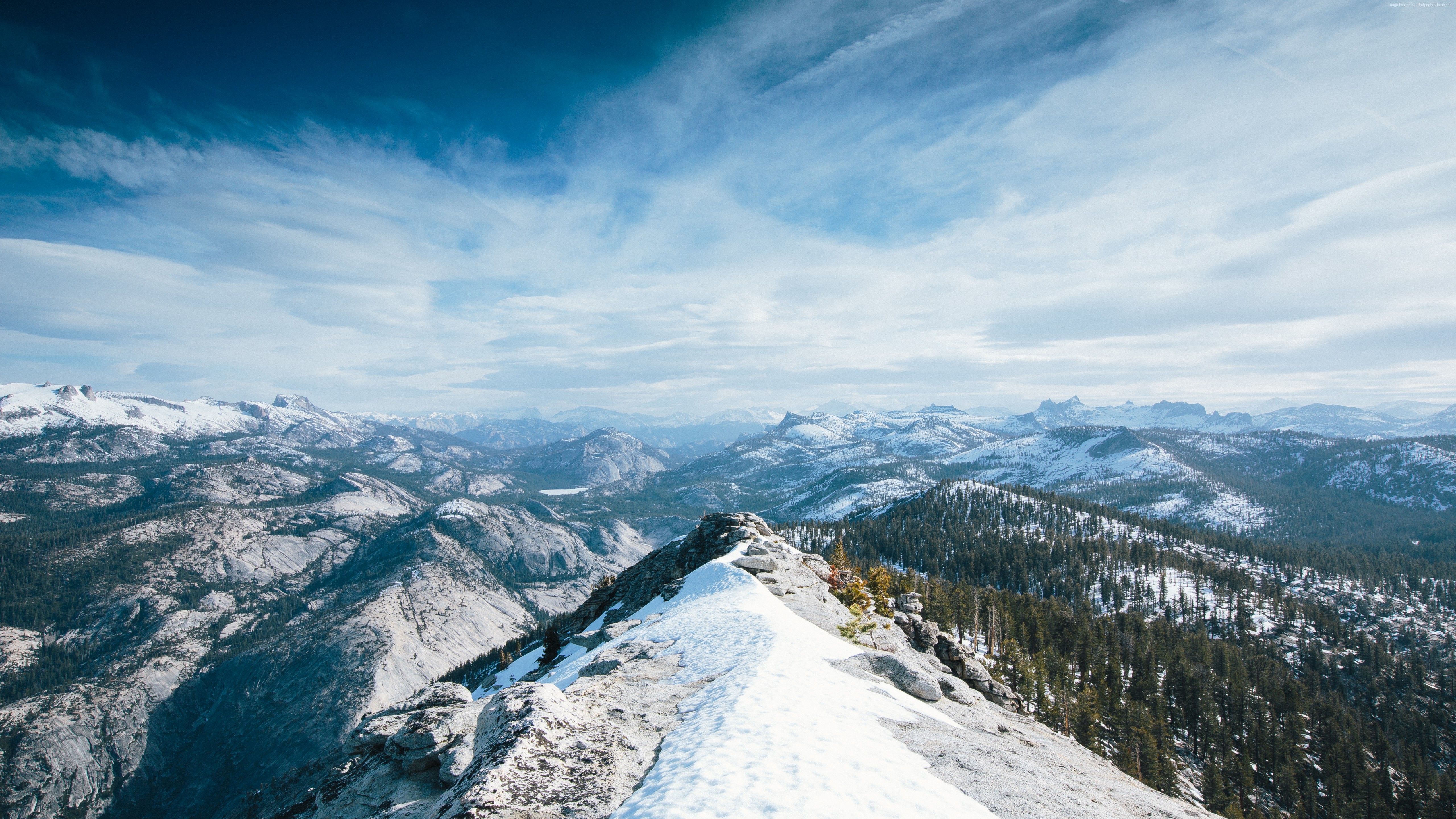 Snowy mountain range with pine trees under a cloudy sky HD Wallpaper