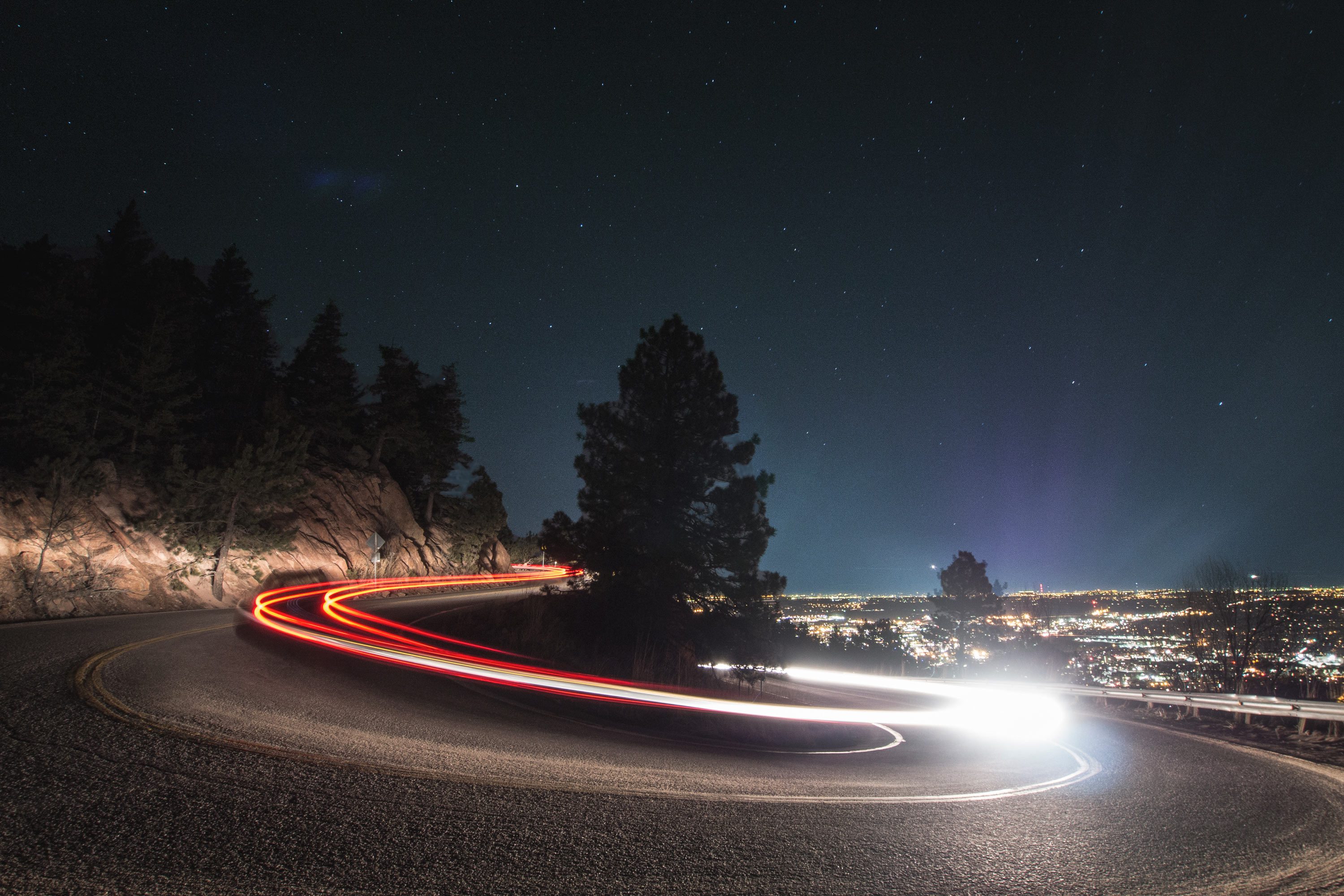 Light painting on a winding road at night with city lights HD Wallpaper