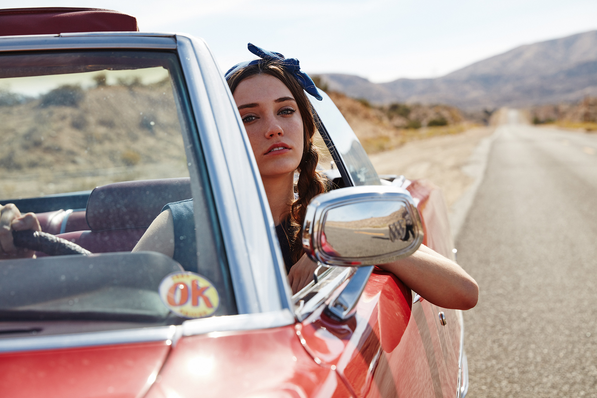 Woman with braids in a red convertible on a desert road HD Wallpaper