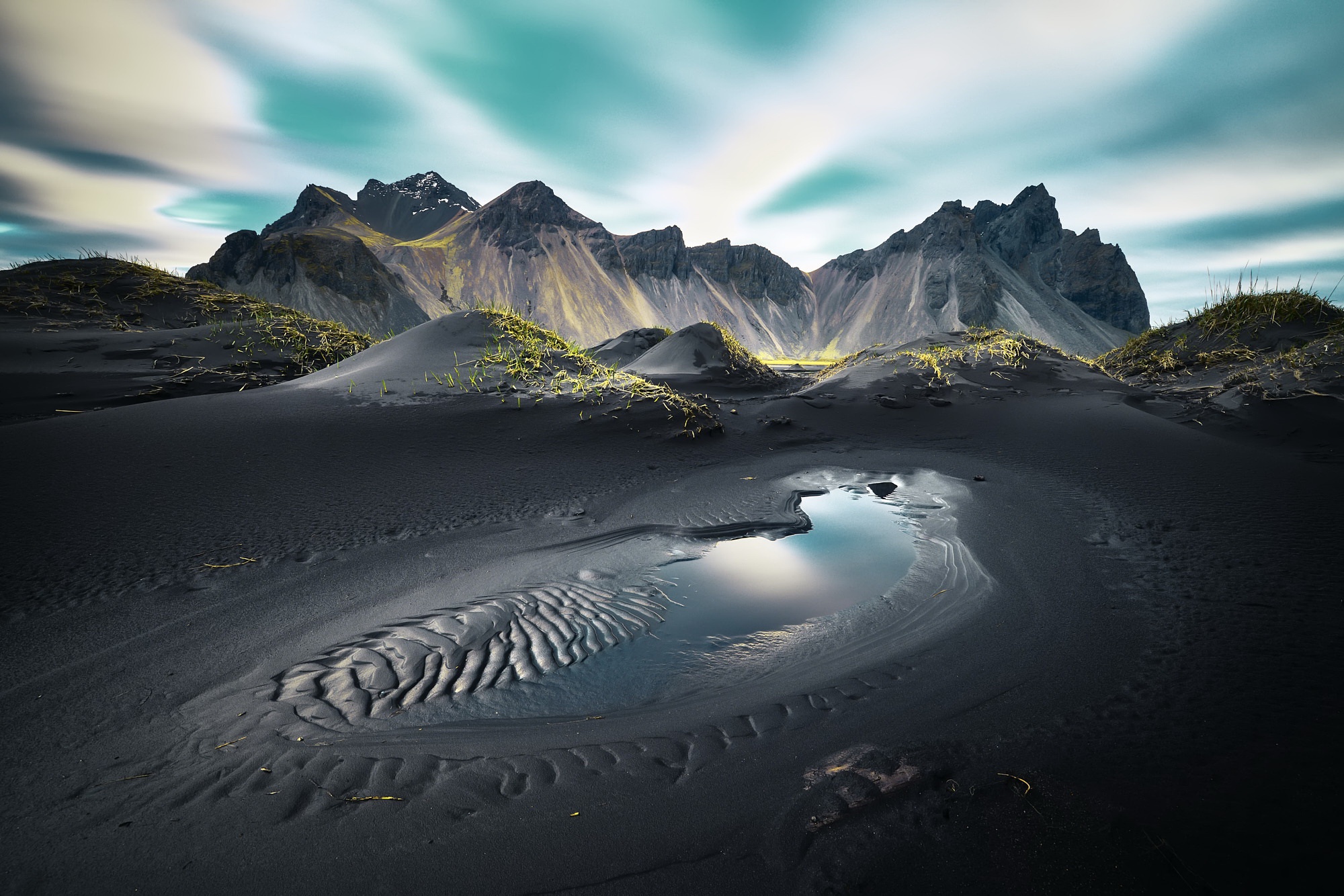 Black sand dunes and mountains under a cloudy sky HD Wallpaper