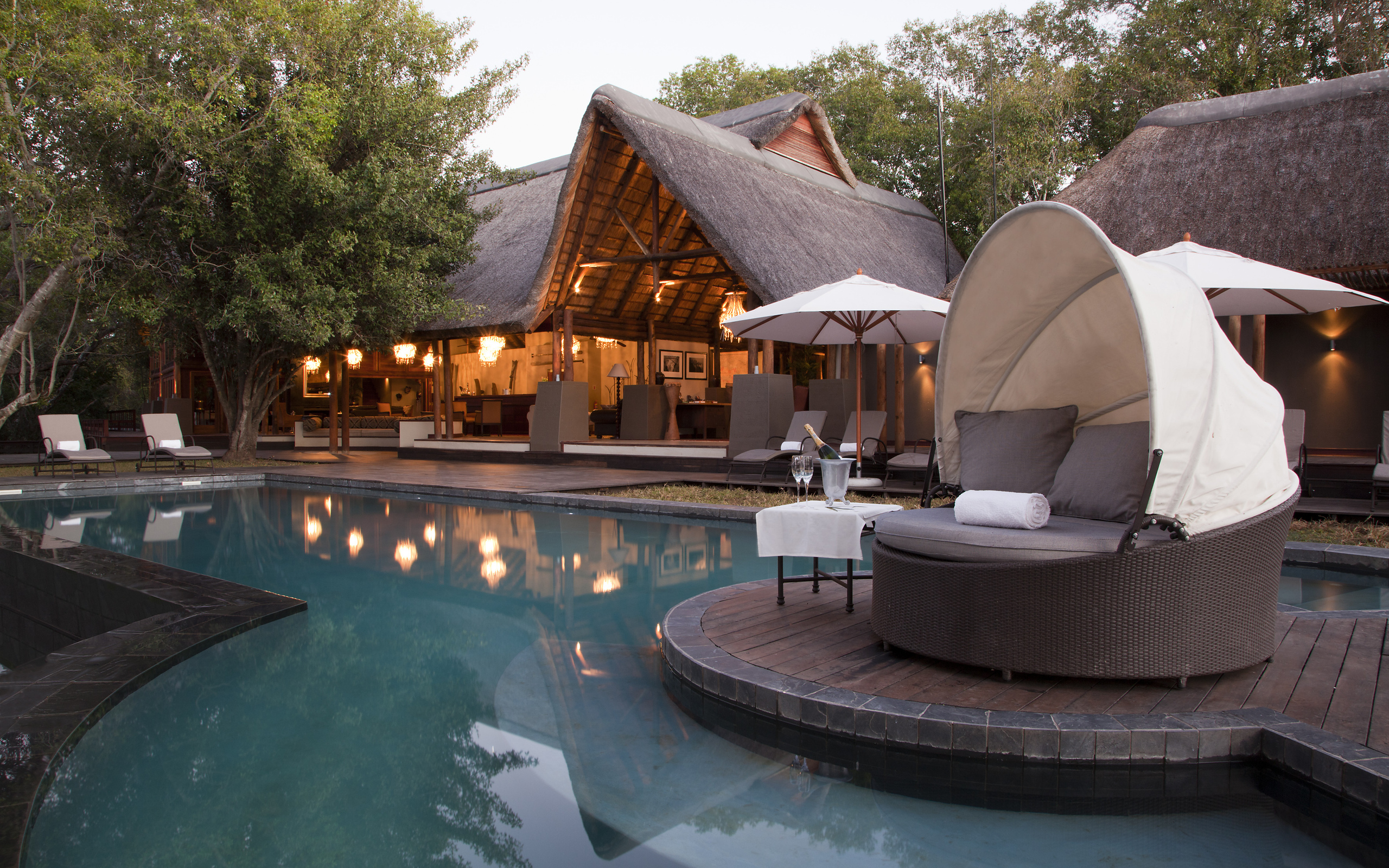 Resort swimming pool with lounge chairs and thatched roof building HD Wallpaper