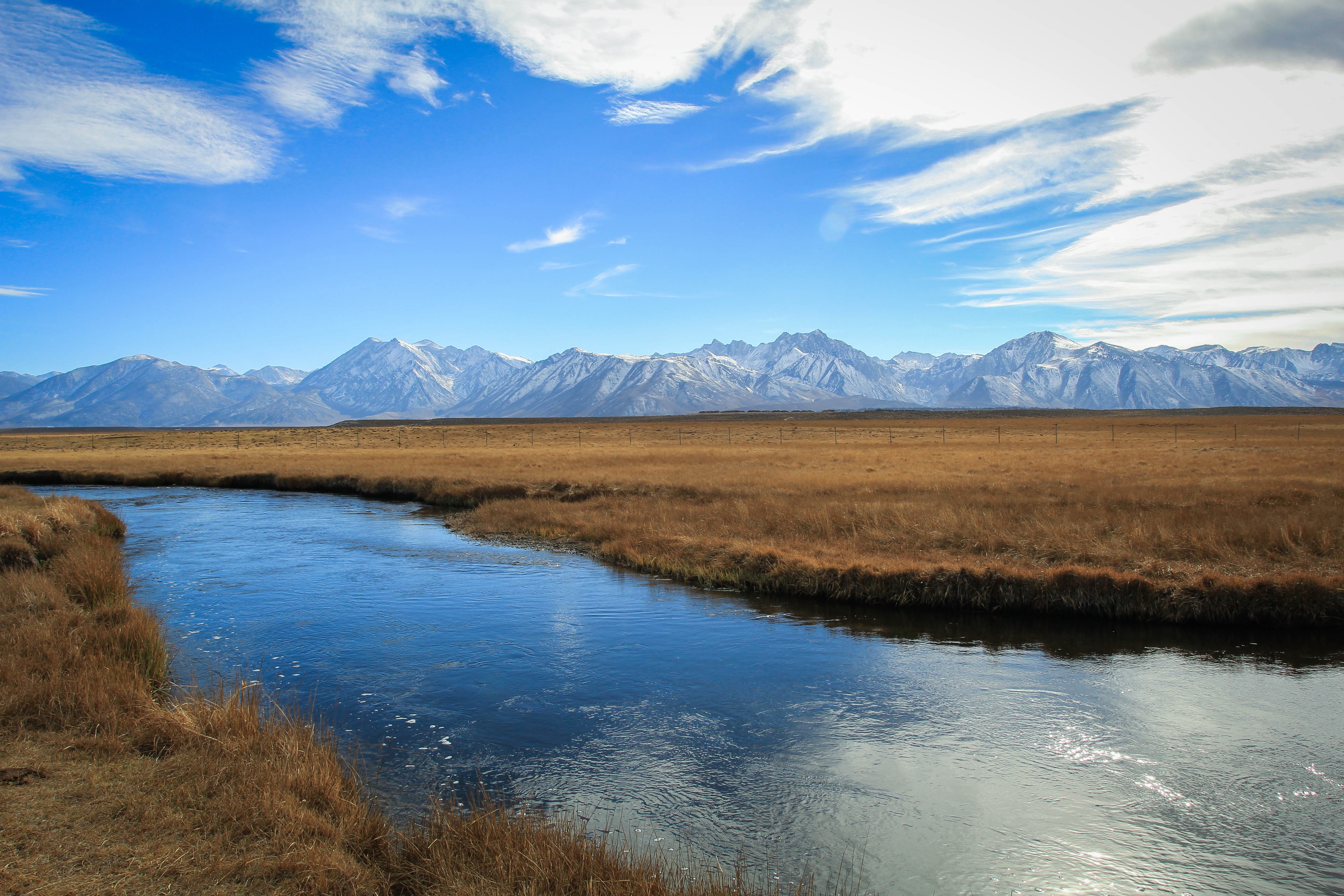 River flowing through a meadow with snow-capped mountains in the background HD Wallpaper