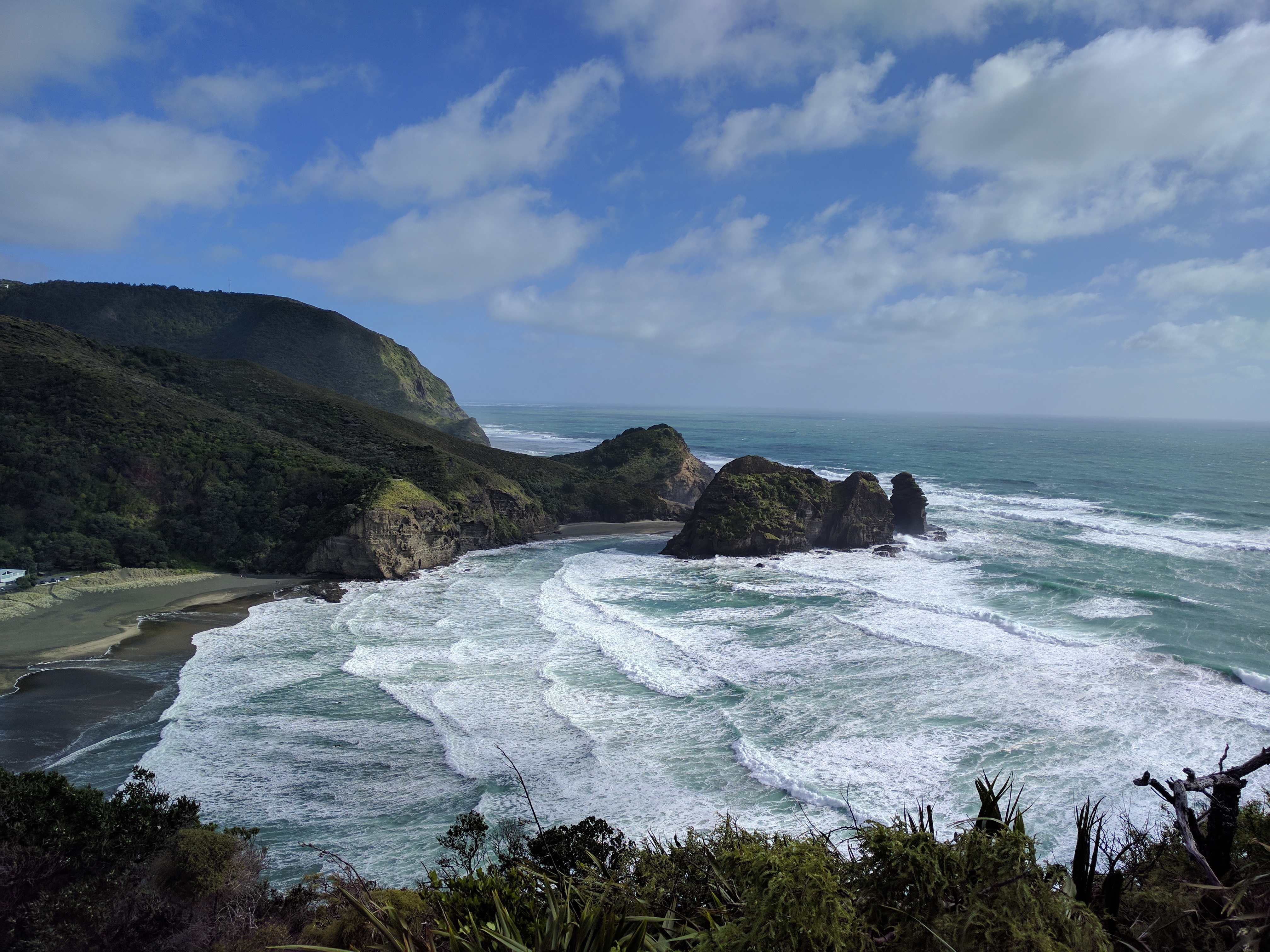 Ocean waves crash on a rocky coastline with green hills HD Wallpaper