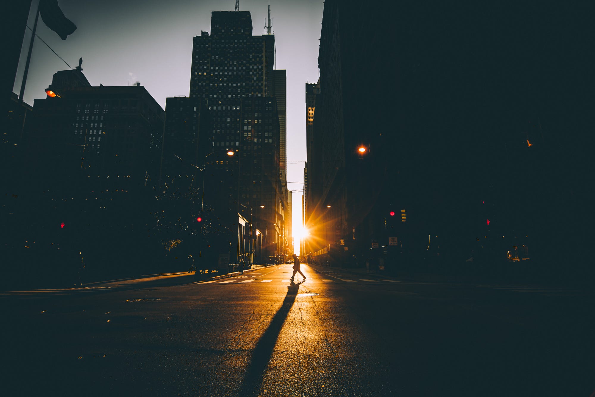 Person crossing street at sunset with skyscrapers HD Wallpaper