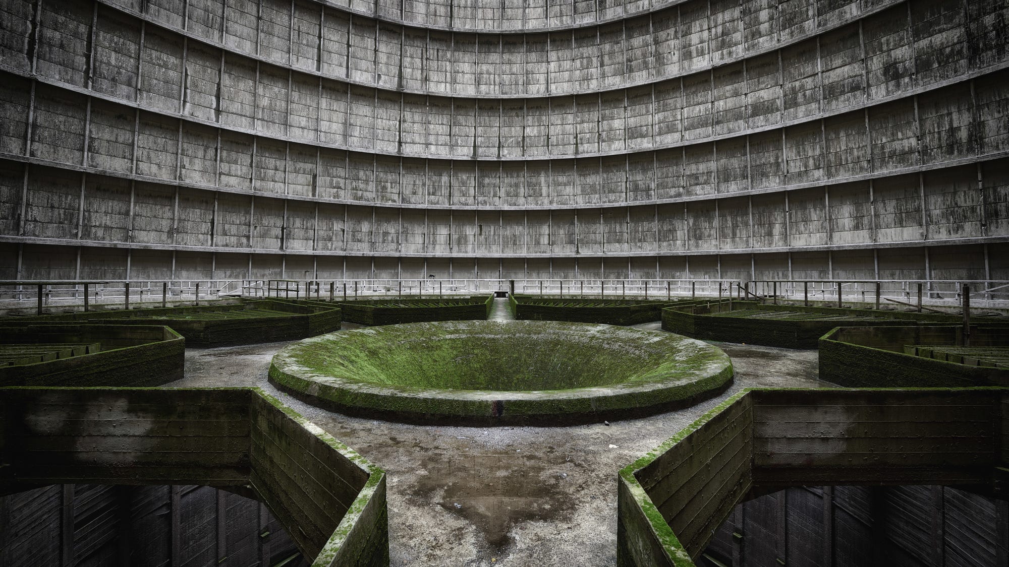 Interior of a large, abandoned concrete cooling tower with moss HD Wallpaper