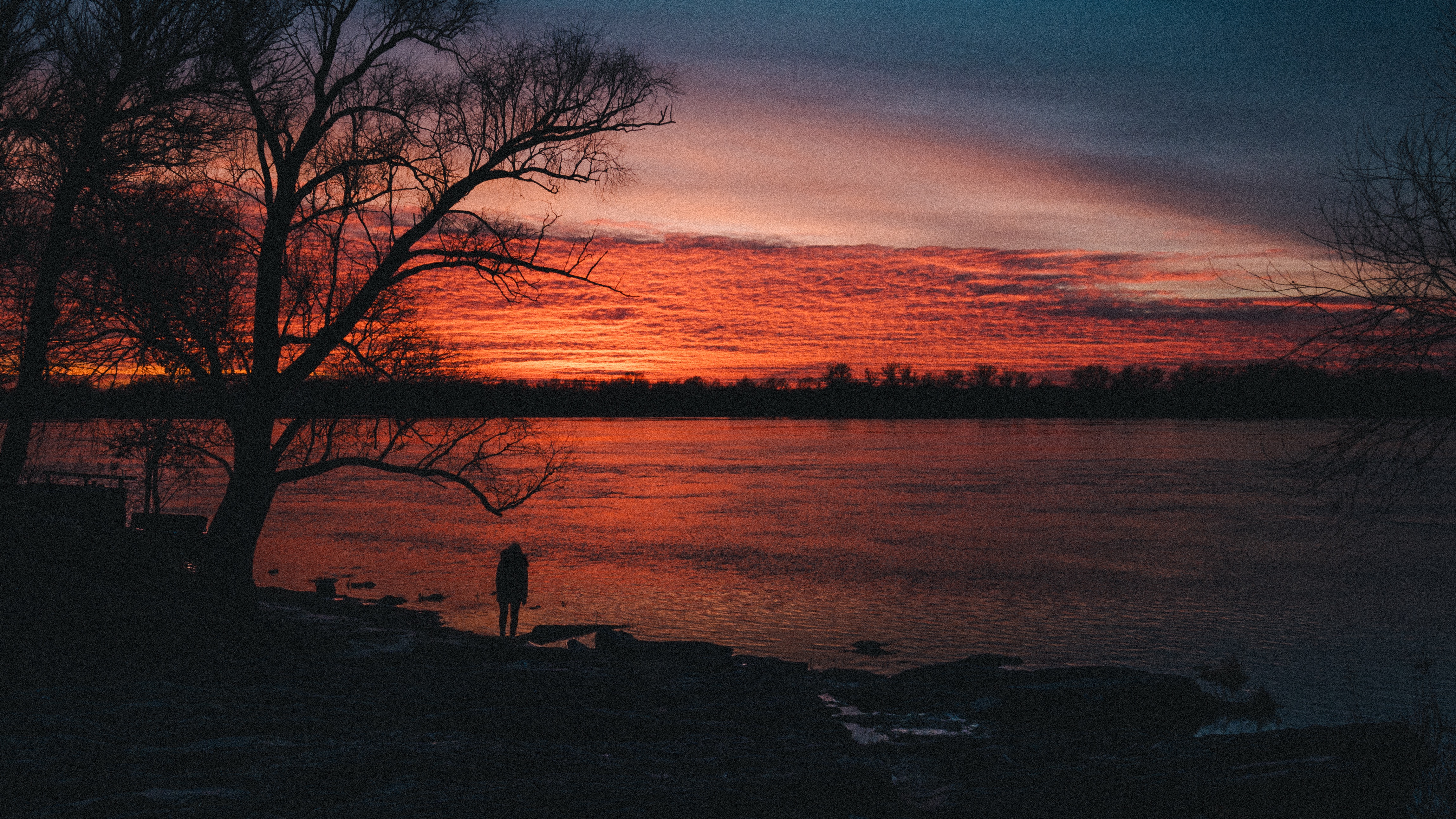 Person standing by a river at sunset HD Wallpaper