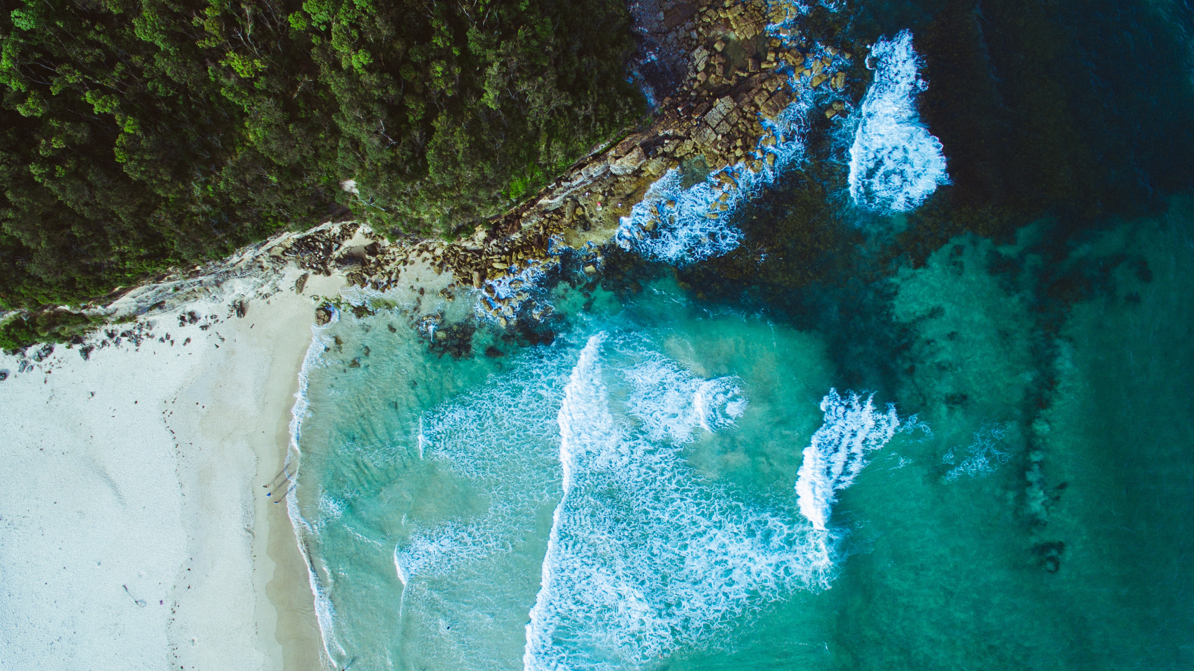 Aerial view of a tropical beach with lush green forest and turquoise ocean waves HD Wallpaper