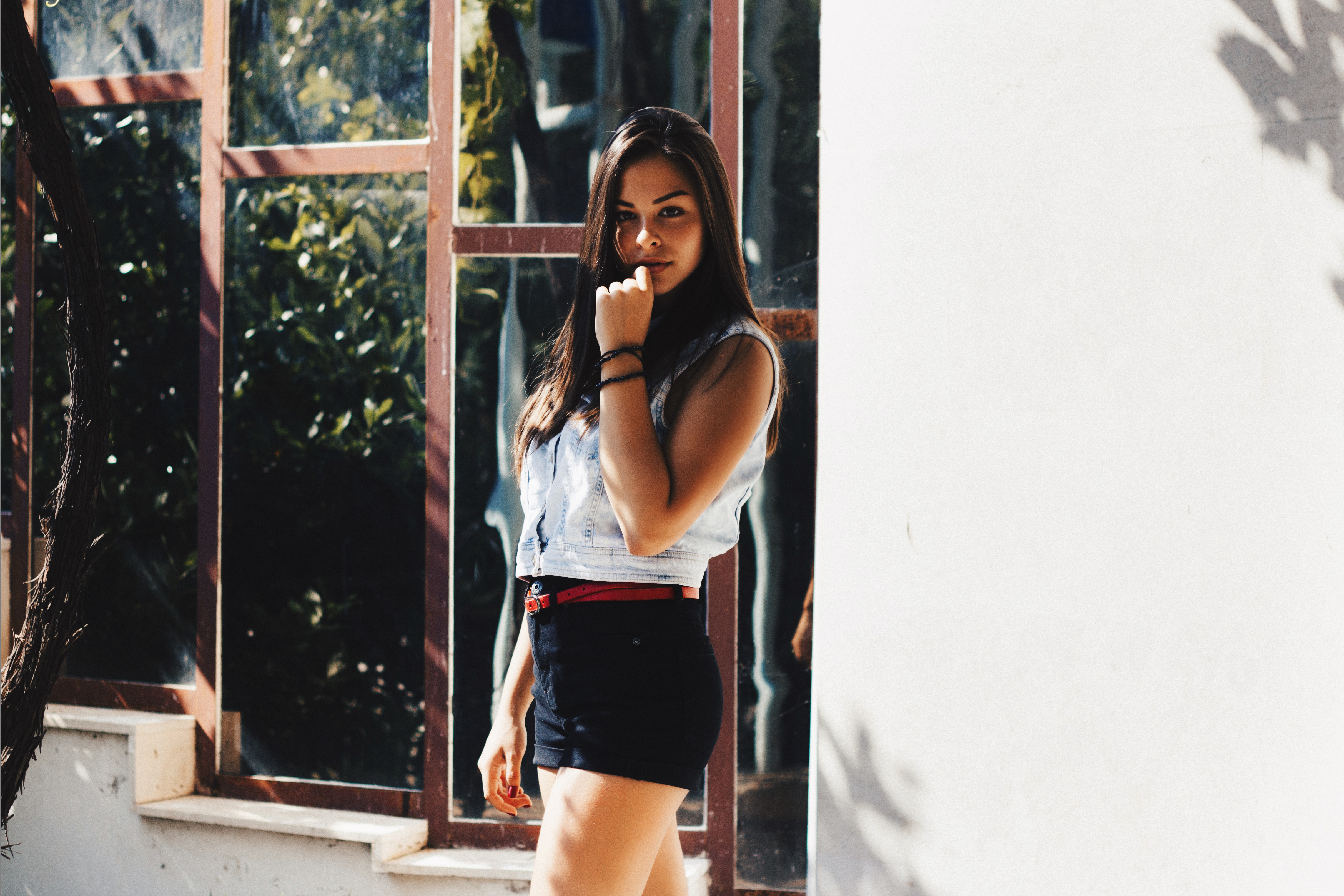 Woman in denim vest and shorts with hand on face HD Wallpaper