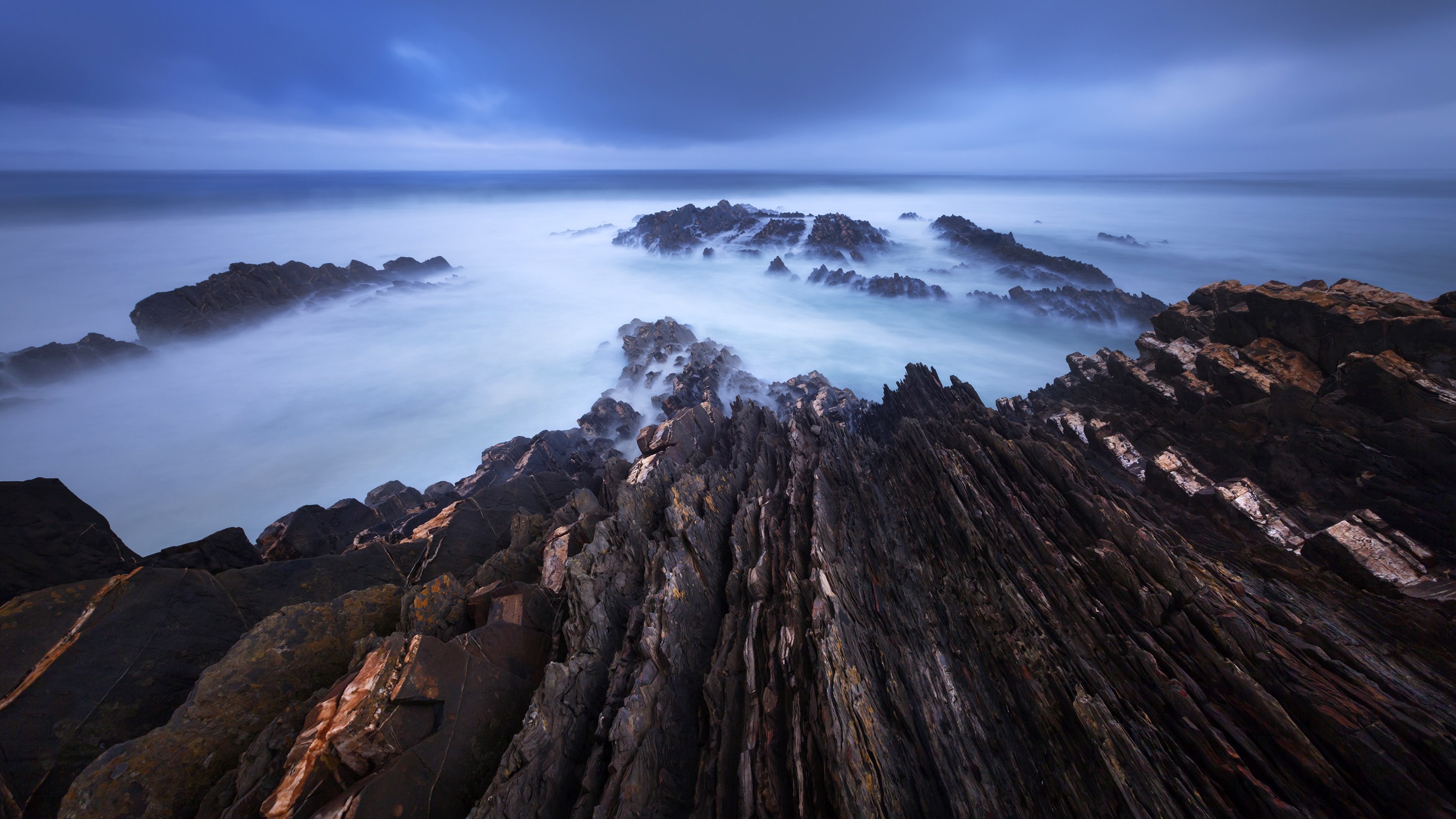 Jagged rocks in misty ocean at dusk HD Wallpaper