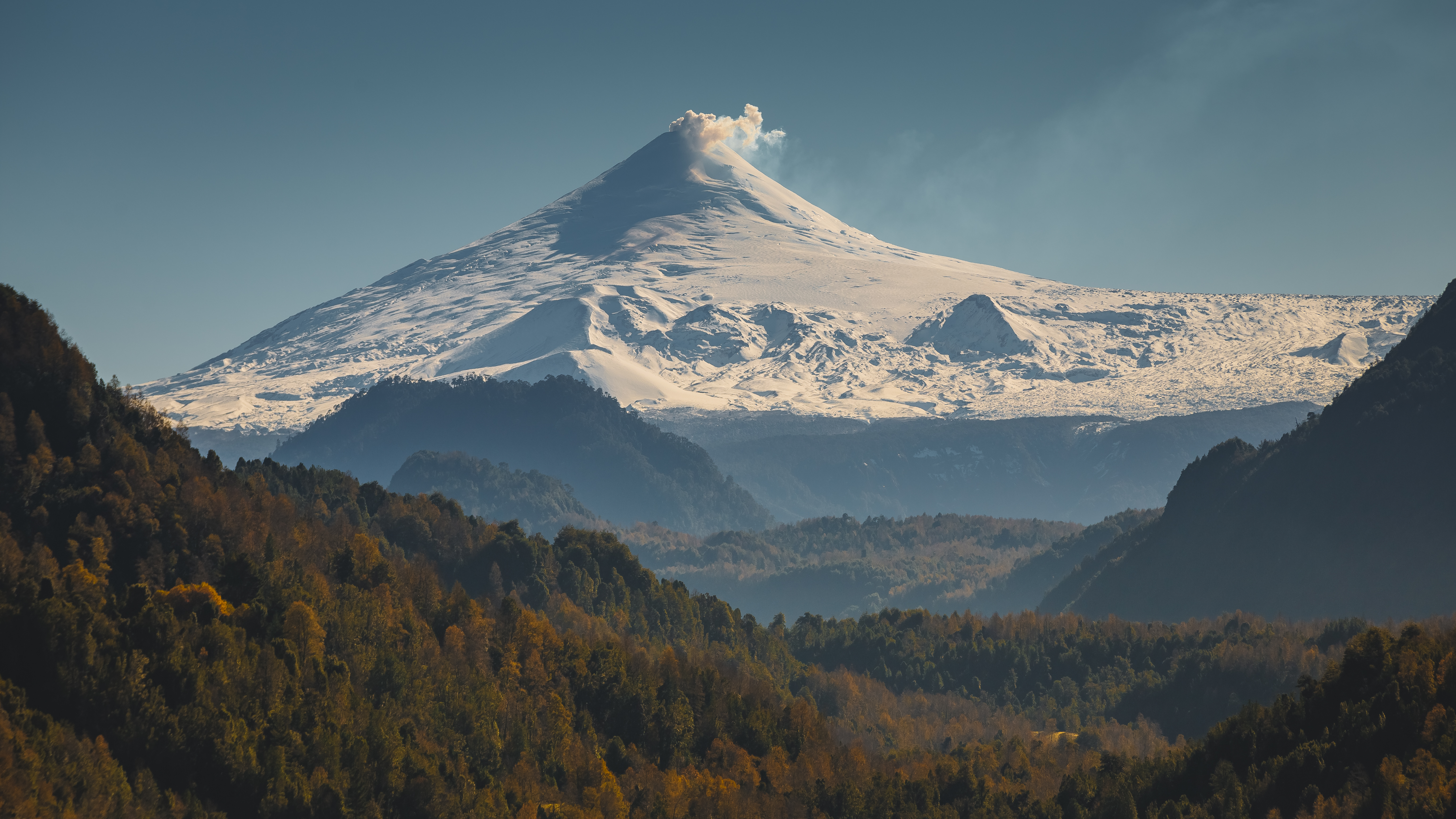 Volcano erupting with smoke over a forest HD Wallpaper