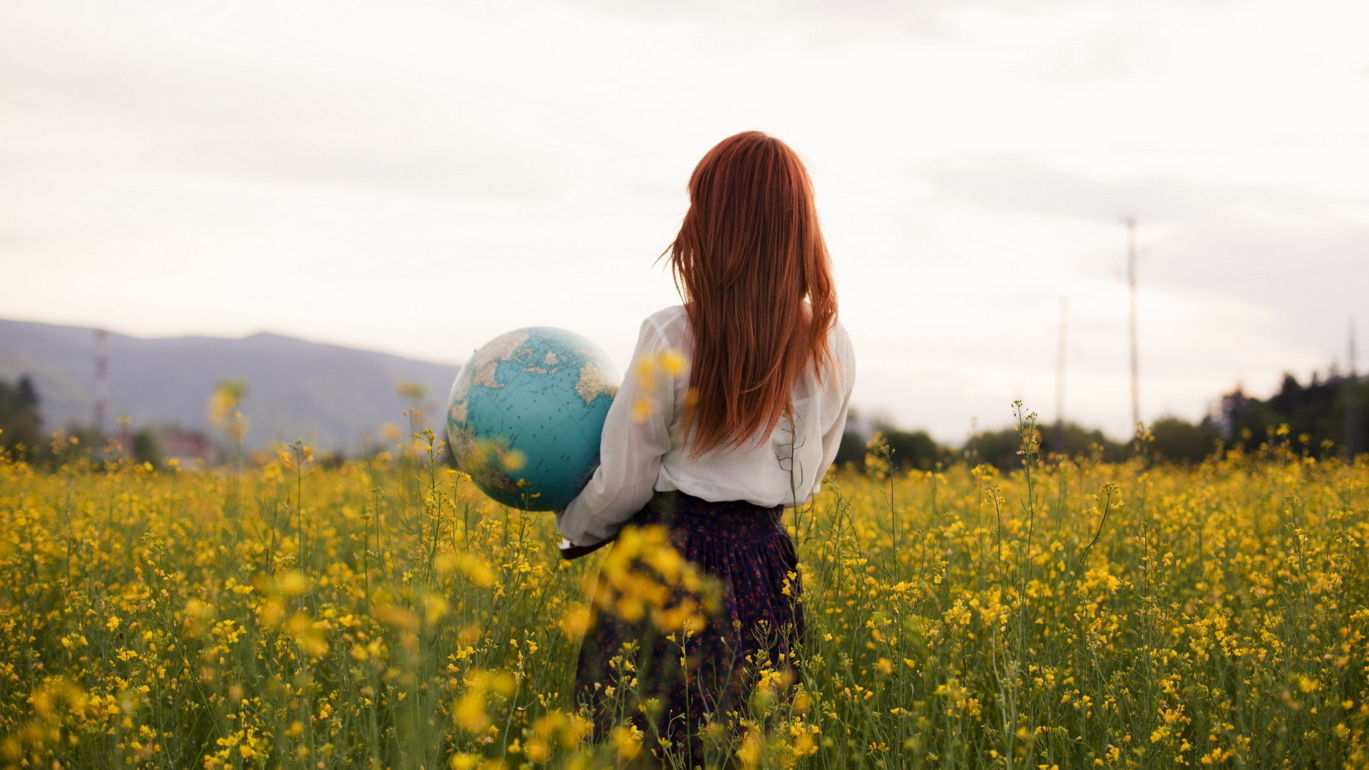 Woman holding a globe in a field of yellow flowers HD Wallpaper