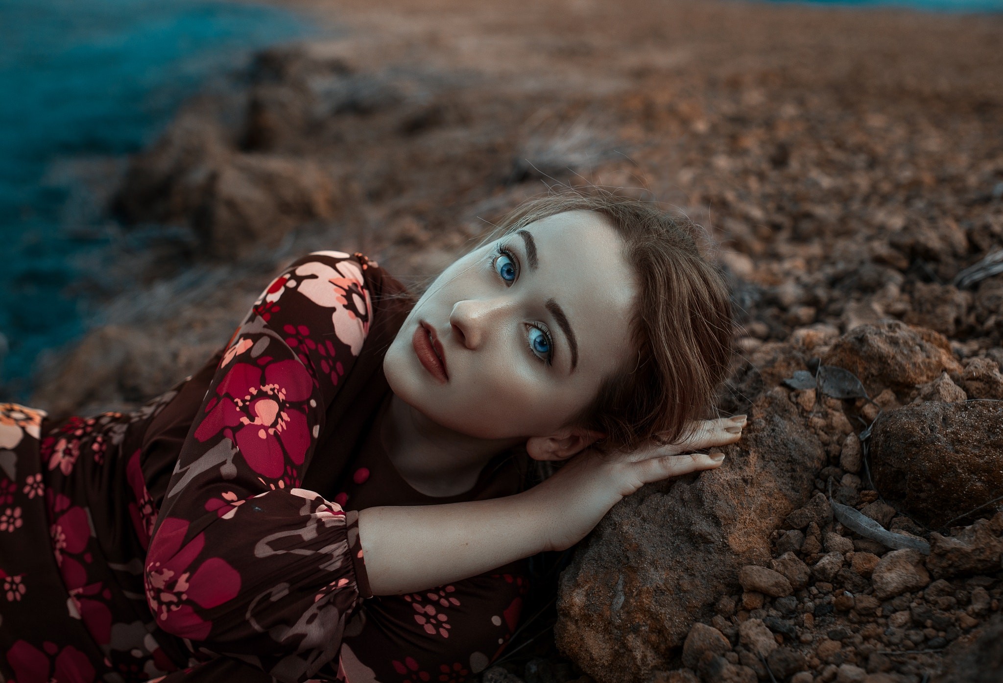 Woman with blue eyes lying on rocks near water HD Wallpaper