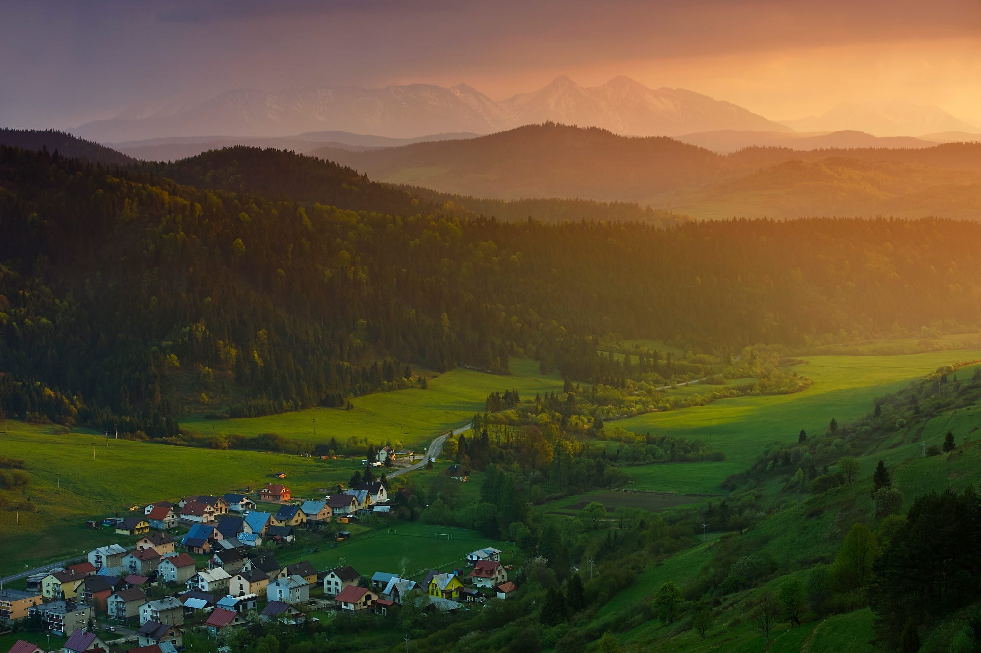Village nestled in a valley with mountains at sunset HD Wallpaper