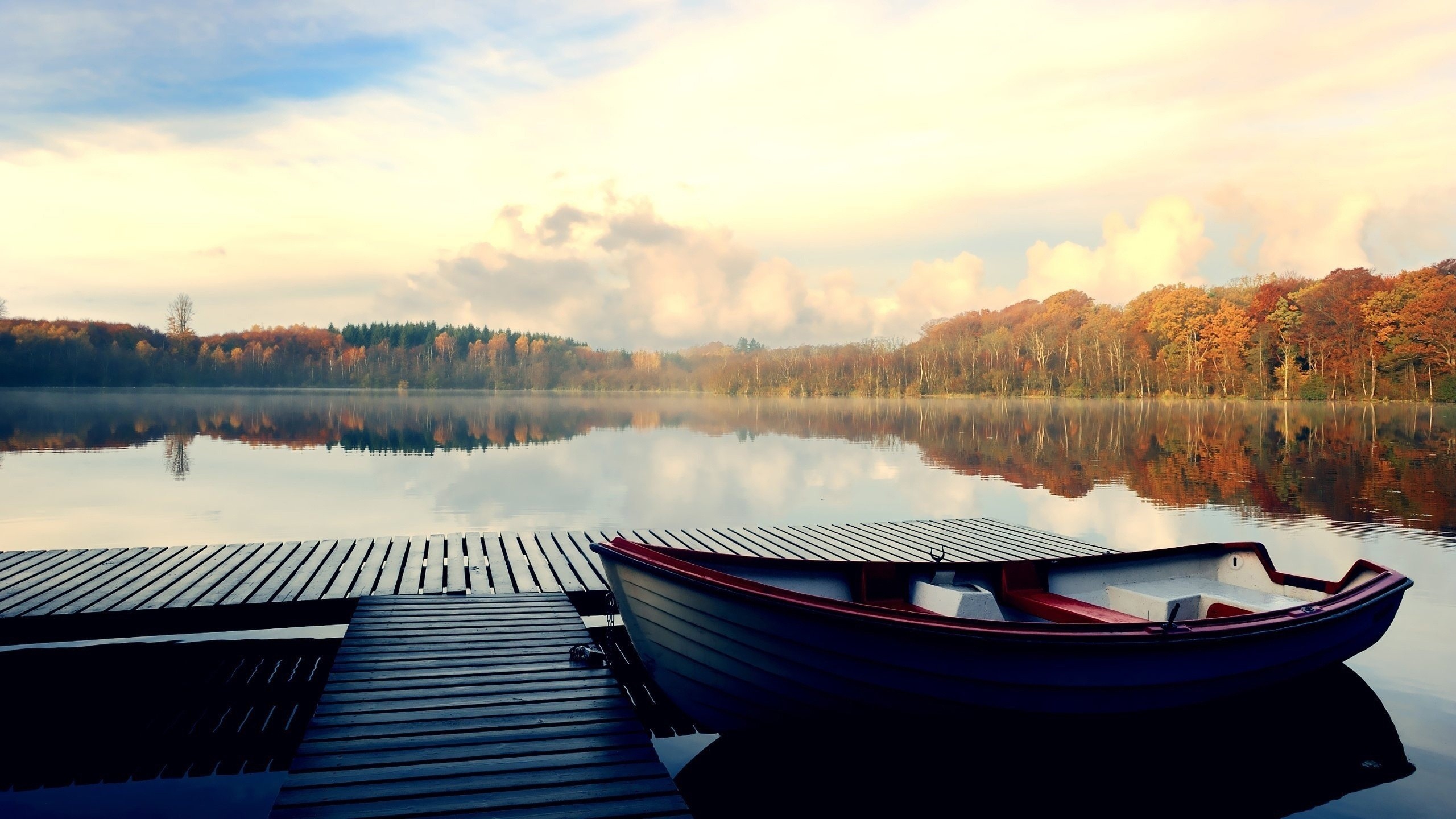 Boat docked at a wooden pier on a calm lake during autumn HD Wallpaper