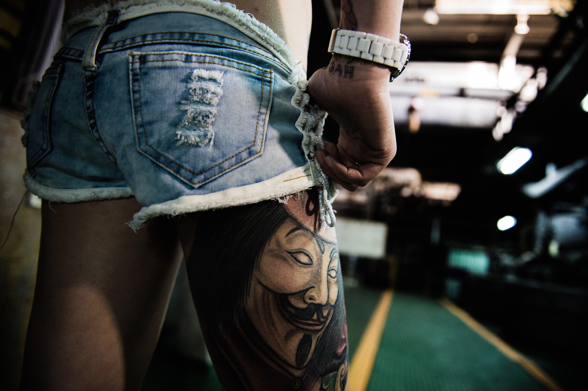 Woman in ripped denim shorts with Anonymous tattoo HD Wallpaper