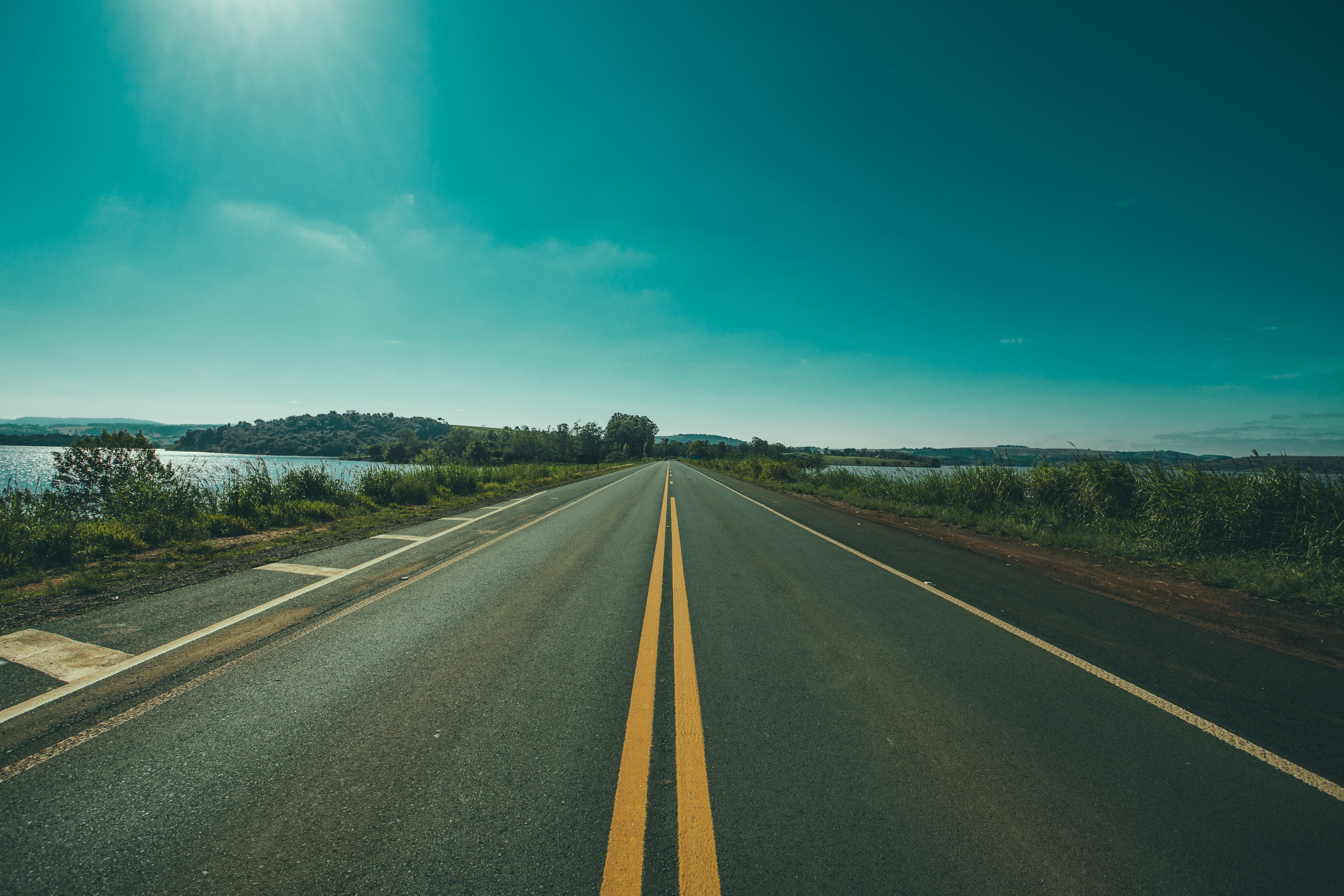 Road with yellow lines next to a body of water HD Wallpaper