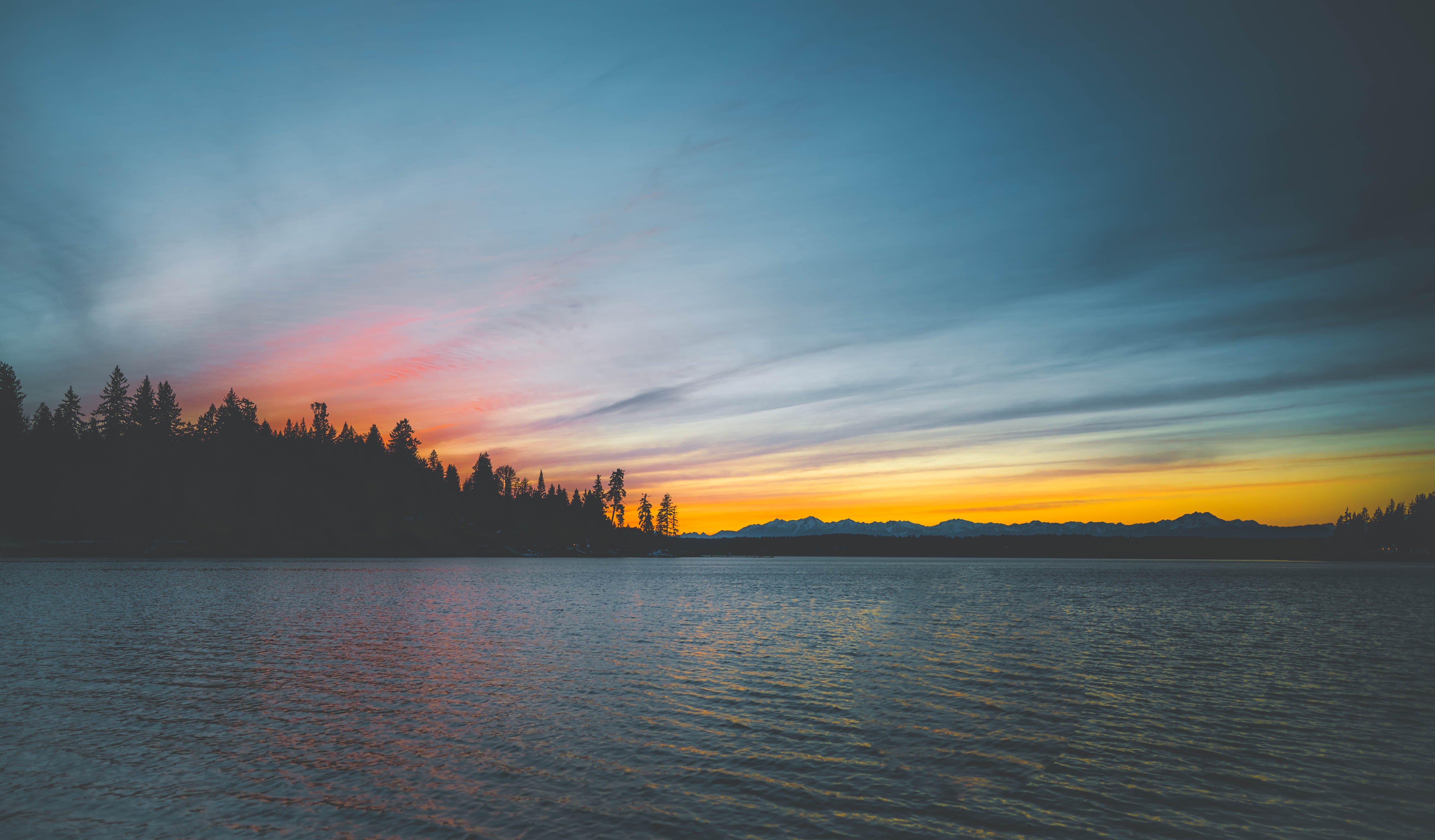 Sunset over a lake with silhouetted trees and mountains HD Wallpaper
